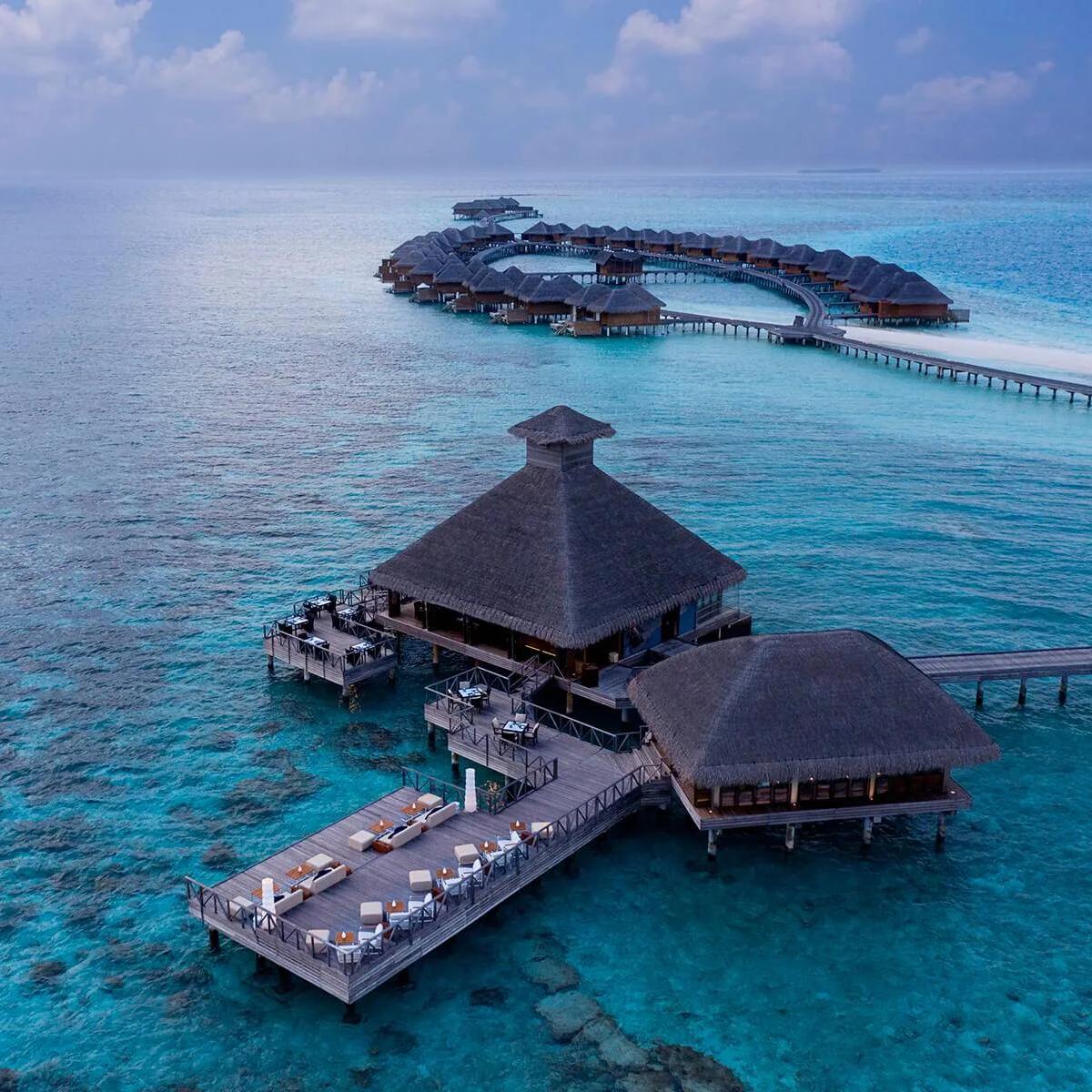 Salt's overwater thatched-roof dining pavilion at dusk, connected by jetty to the resort's row of villas