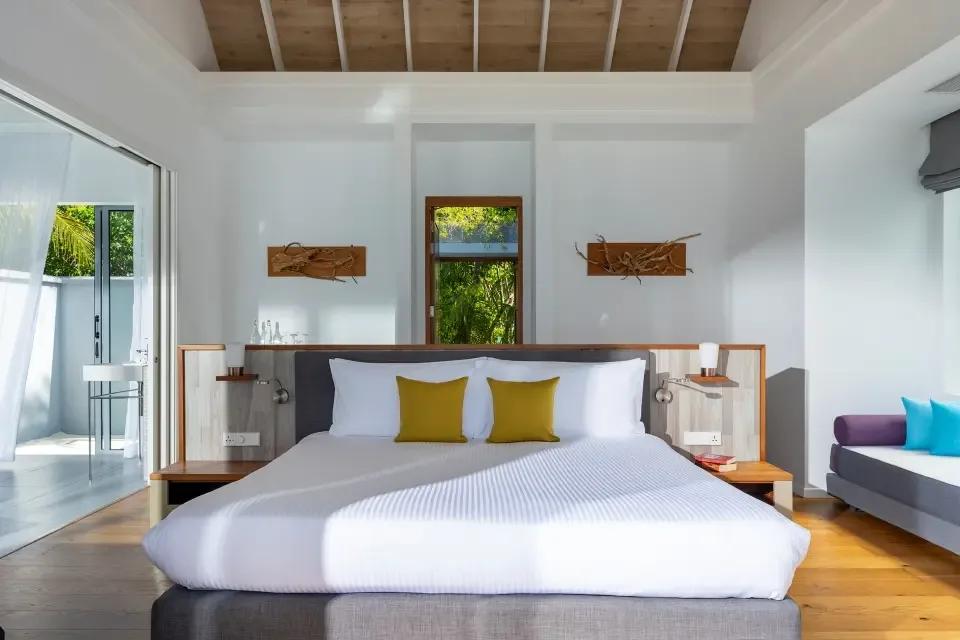 Pool Villa bedroom with a grey upholstered bed base, mustard cushions, and warm wood-panelled ceiling