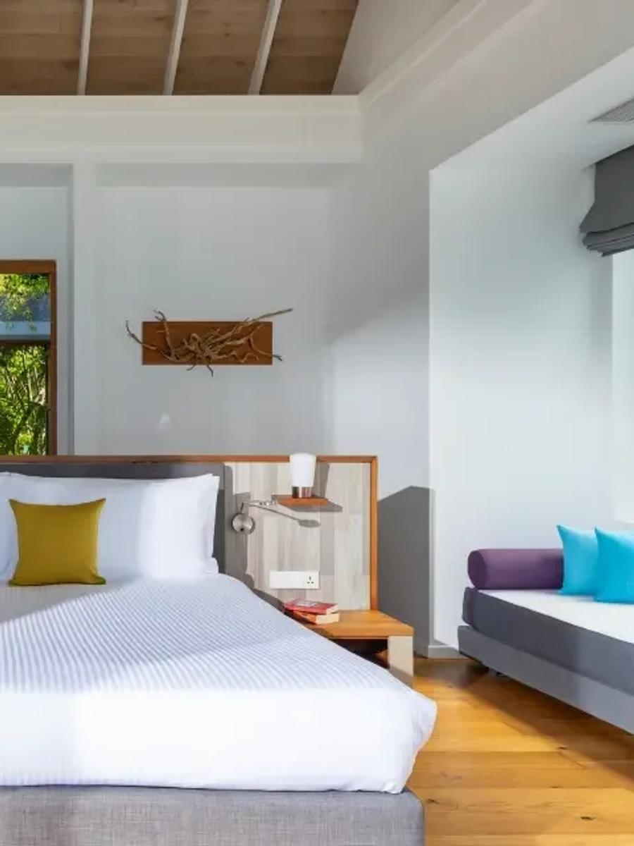 Pool Villa bedroom with a grey upholstered bed base, mustard cushions, and warm wood-panelled ceiling