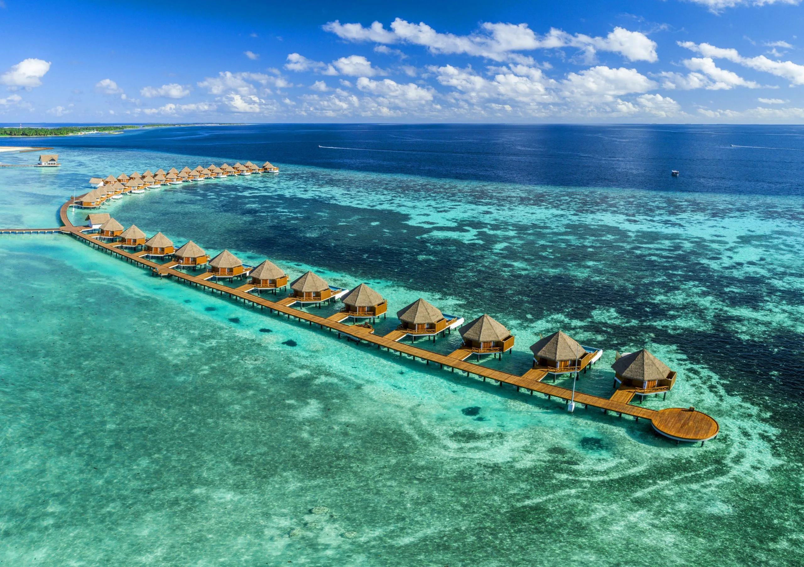 A row of Overwater Villas at Mercure Maldives Kooddoo Resort, framed by the lagoon and reef beyond
