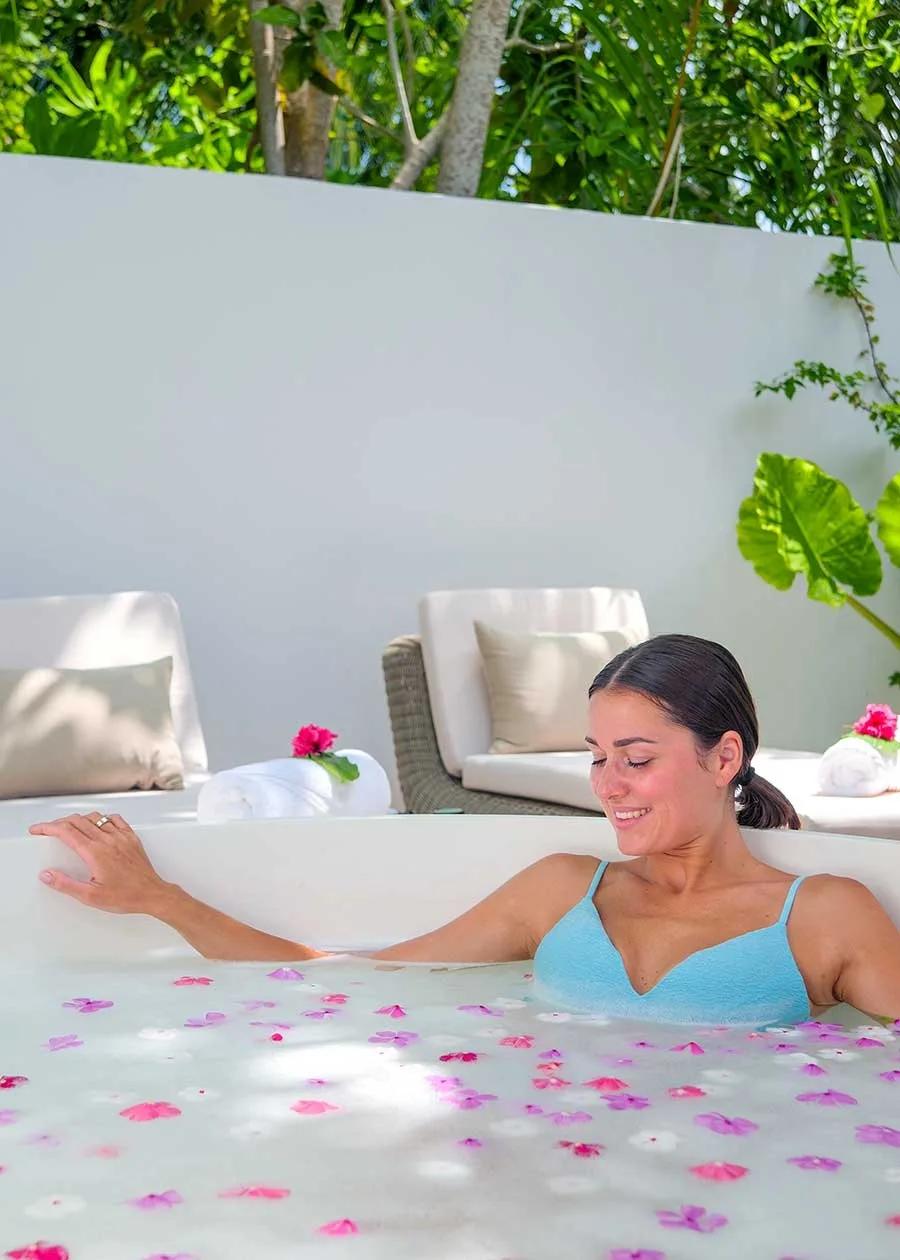A guest resting in an outdoor flower-petal bath at Aura Spa, Baglioni Maldives
