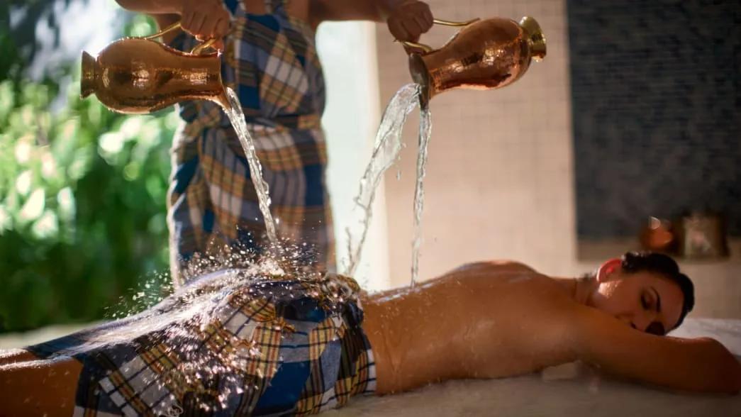 A therapist pouring warm water over a guest's back during a treatment at Balance Wellness