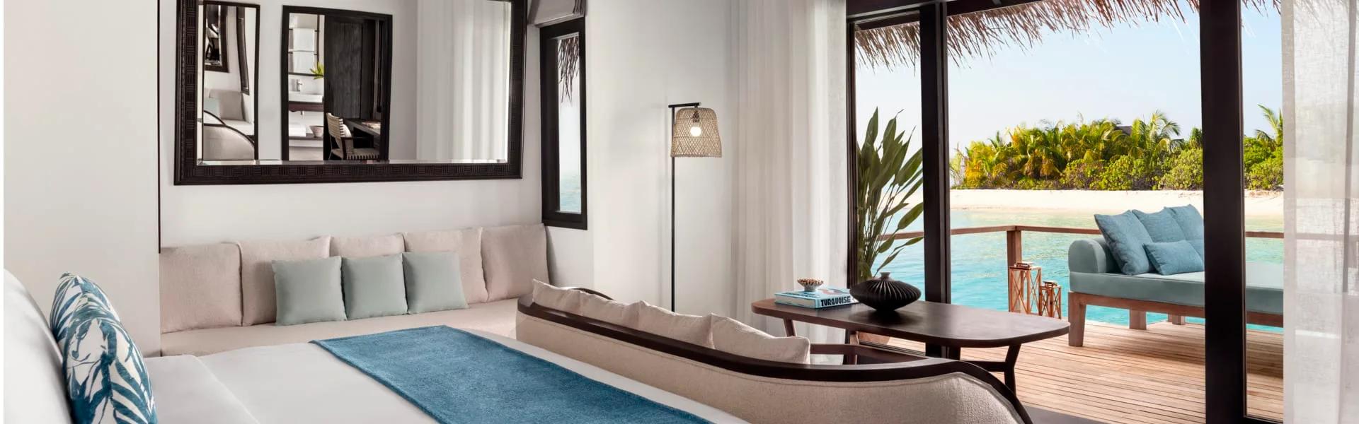 Deluxe Over Water Villa bedroom and lounge with a mirrored dressing area and lagoon-facing deck
