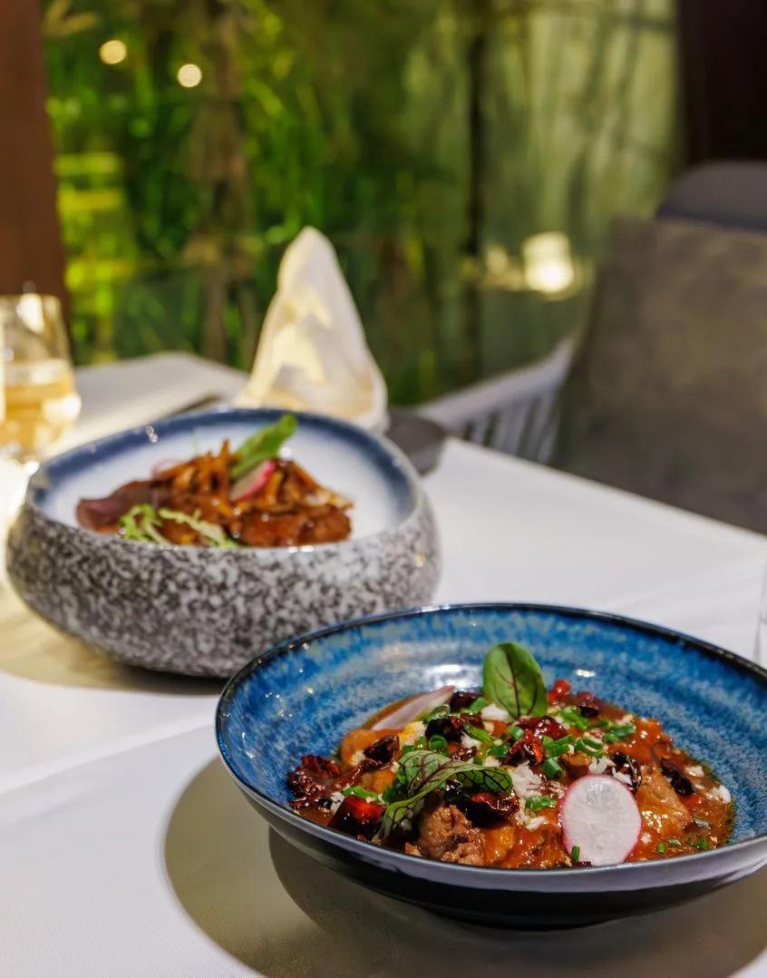 Two plated pan-Asian dishes garnished with radish and herbs on a candlelit table at Soyi