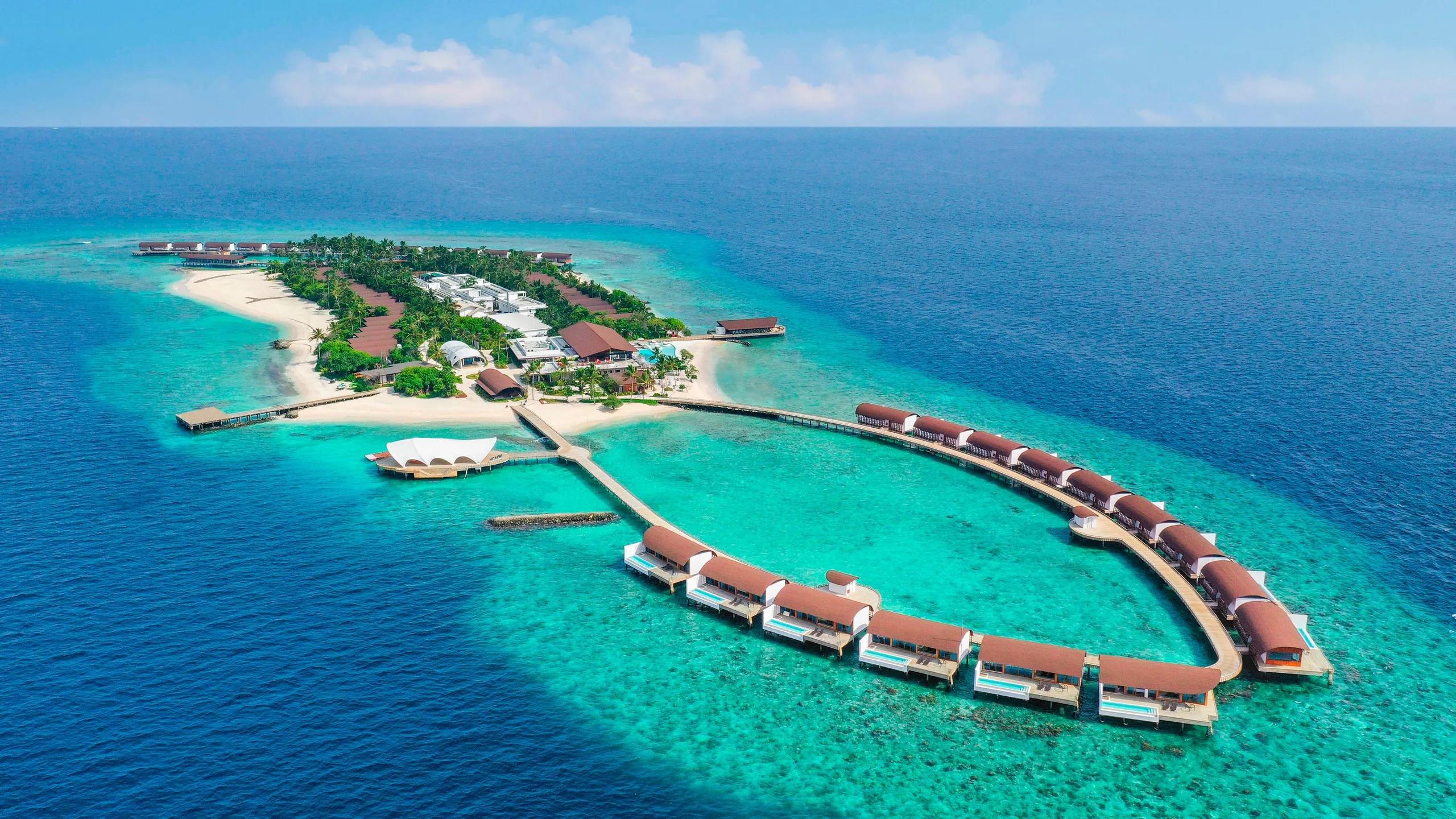 The Westin Maldives Miriandhoo Resort from above — beach villas and the main pool connected by a jetty to a ring of overwater villas in Baa Atoll