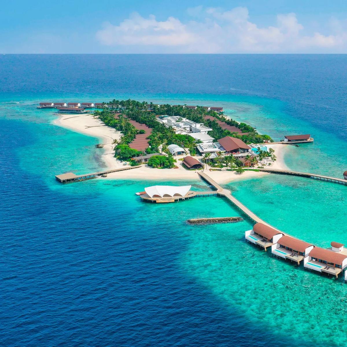 The Westin Maldives Miriandhoo Resort from above — beach villas and the main pool connected by a jetty to a ring of overwater villas in Baa Atoll