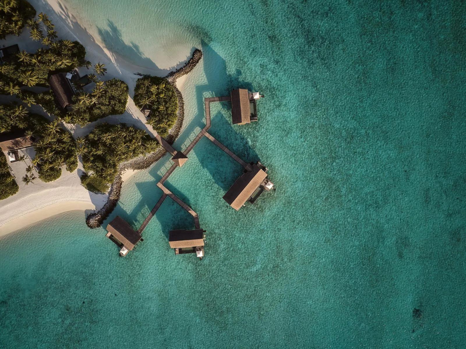 Aerial view of four Grand Water Villas at One&Only Reethi Rah, linked by a zigzag walkway over the reef