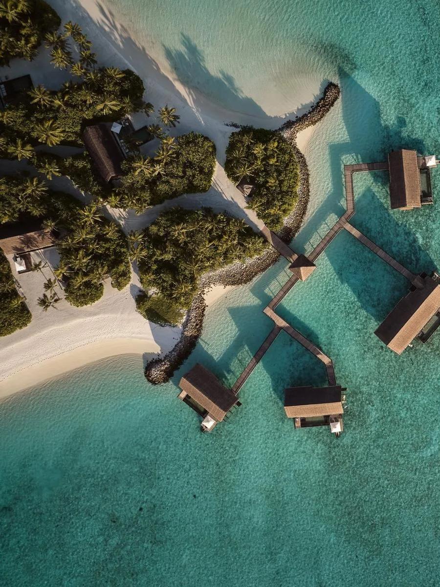 Aerial view of four Grand Water Villas at One&Only Reethi Rah, linked by a zigzag walkway over the reef