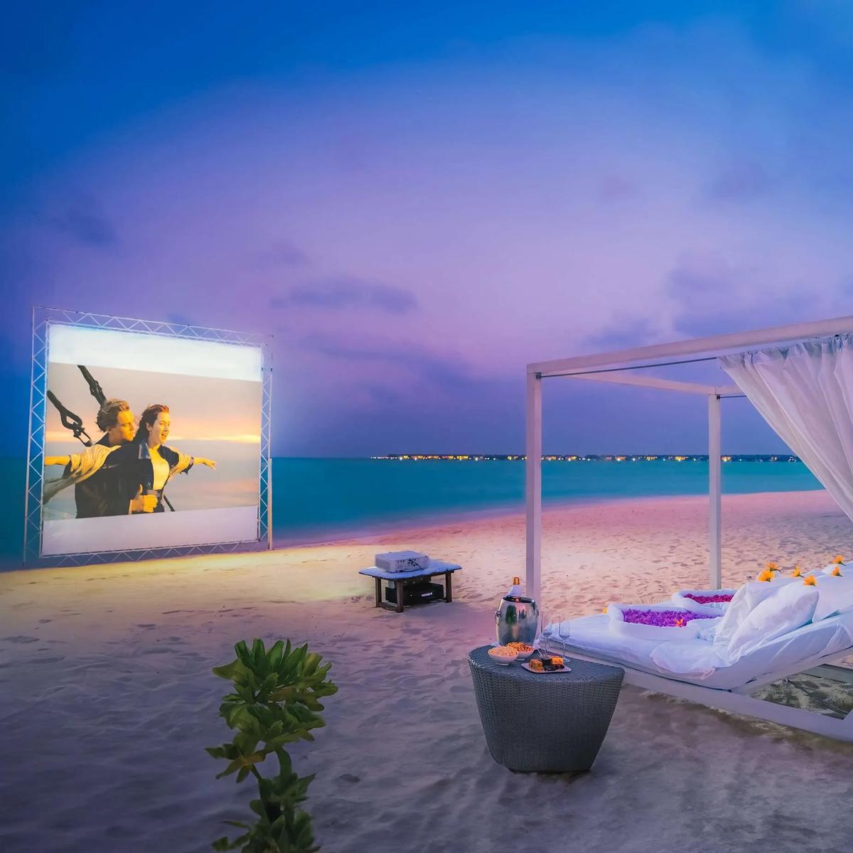 An outdoor cinema screening on the beach at dusk, daybed seating and champagne set up in front, Hideaway Beach Resort & Spa