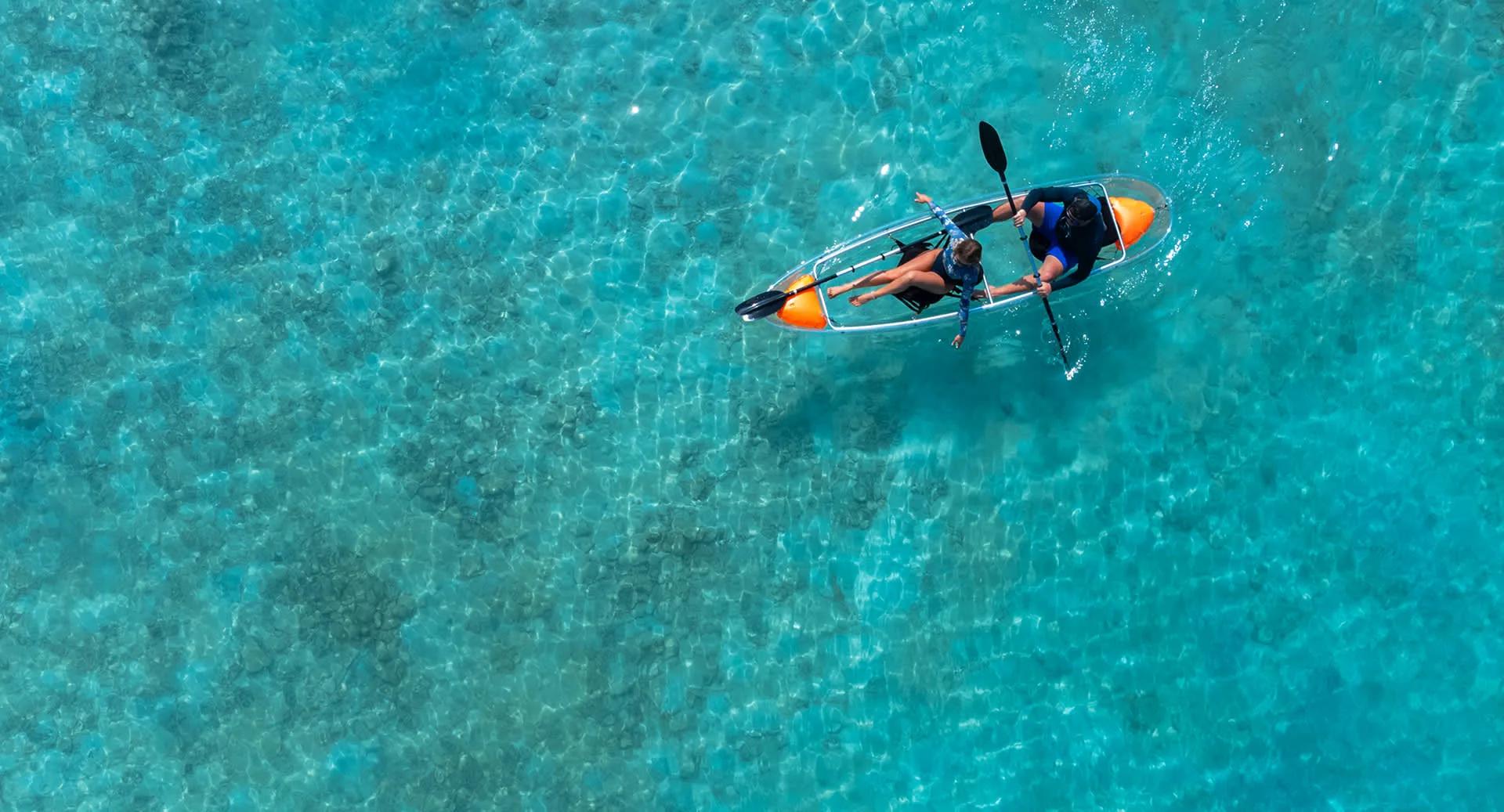 A glass-bottomed canoe crossing the resort's clear lagoon, the reef floor visible beneath