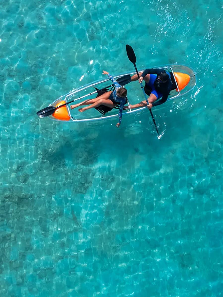 A glass-bottomed canoe crossing the resort's clear lagoon, the reef floor visible beneath