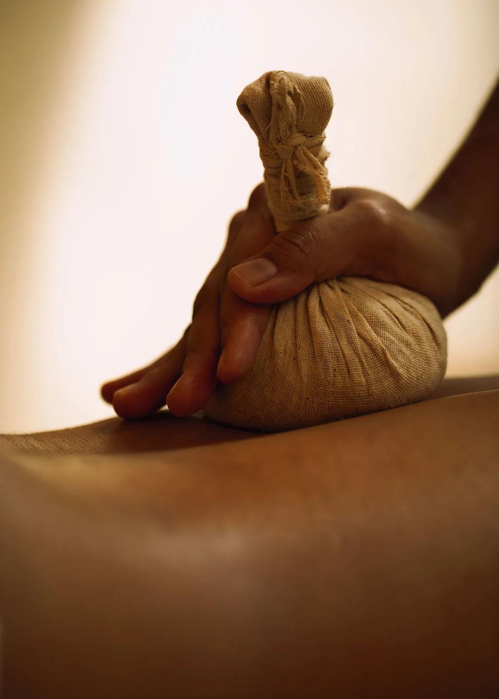 A therapist presses a warm herbal compress into a guest's back during a treatment at Soneva Soul