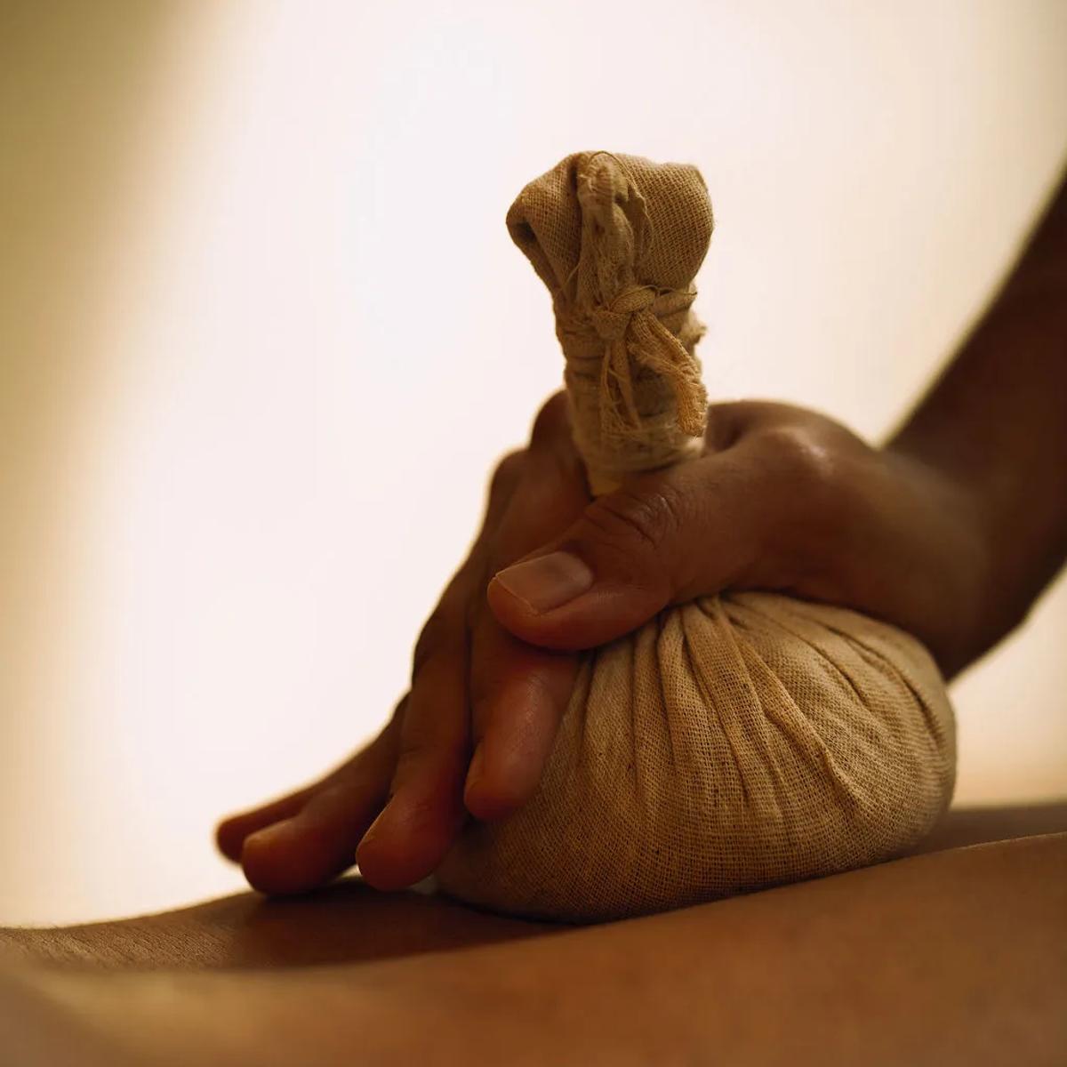 A therapist presses a warm herbal compress into a guest's back during a treatment at Soneva Soul