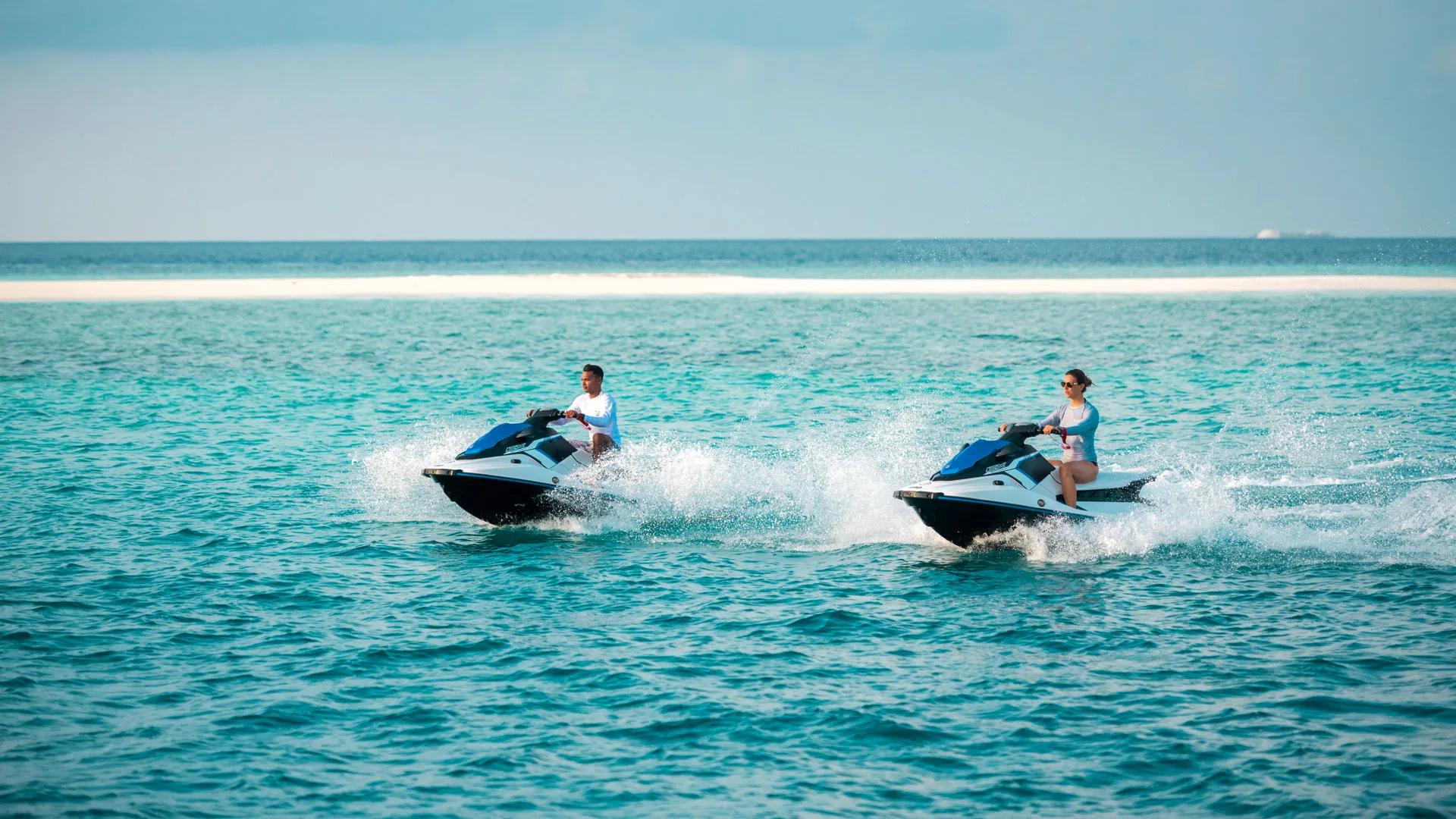 Two riders on jet skis crossing the lagoon with a sandbank in the distance