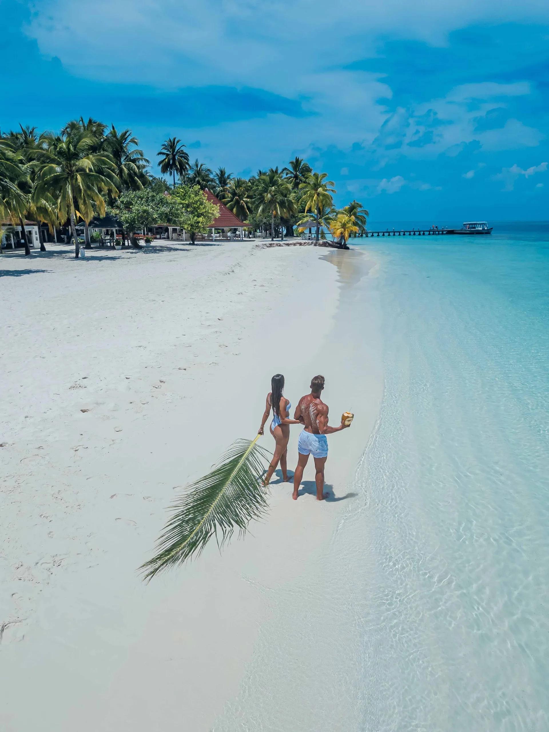 A couple walking the beach at Diamonds Athuruga, the water villa jetty behind them