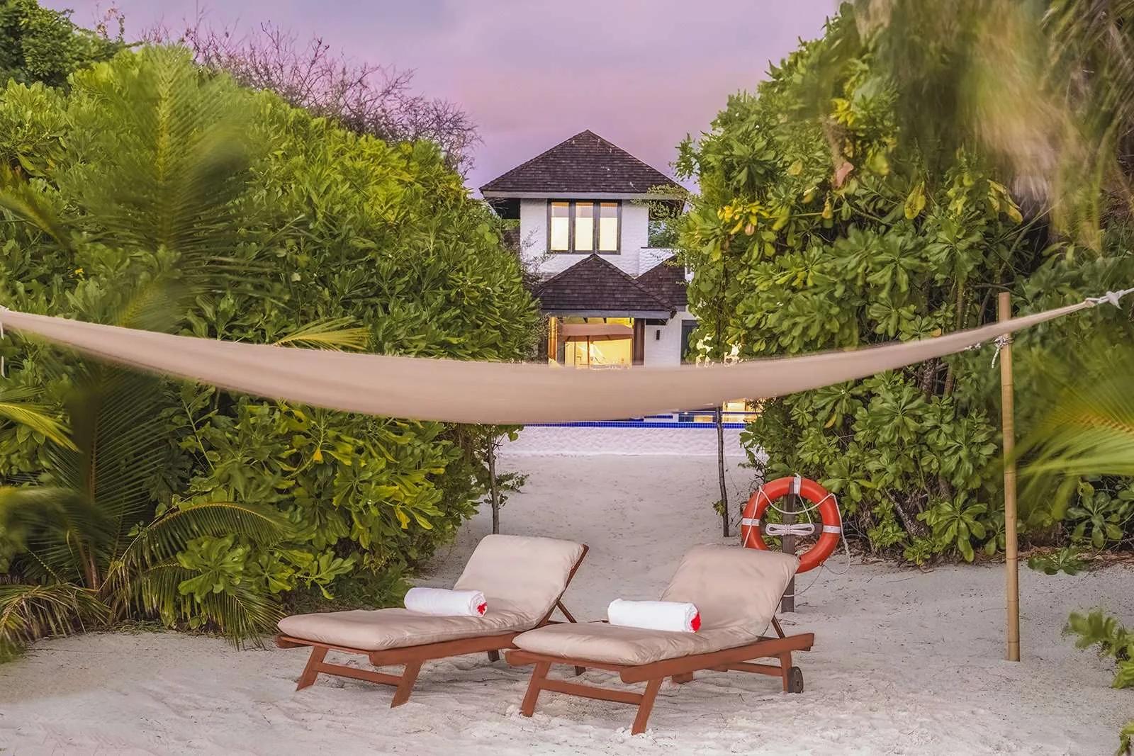 A two-storey Sunset Beach Residence with Pool at dusk, seen through palm trees from the beach