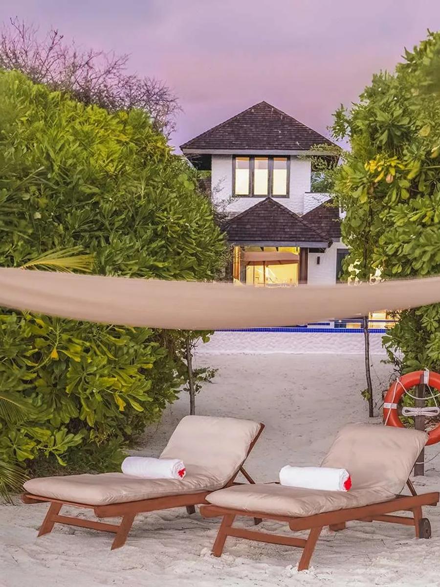 A two-storey Sunset Beach Residence with Pool at dusk, seen through palm trees from the beach