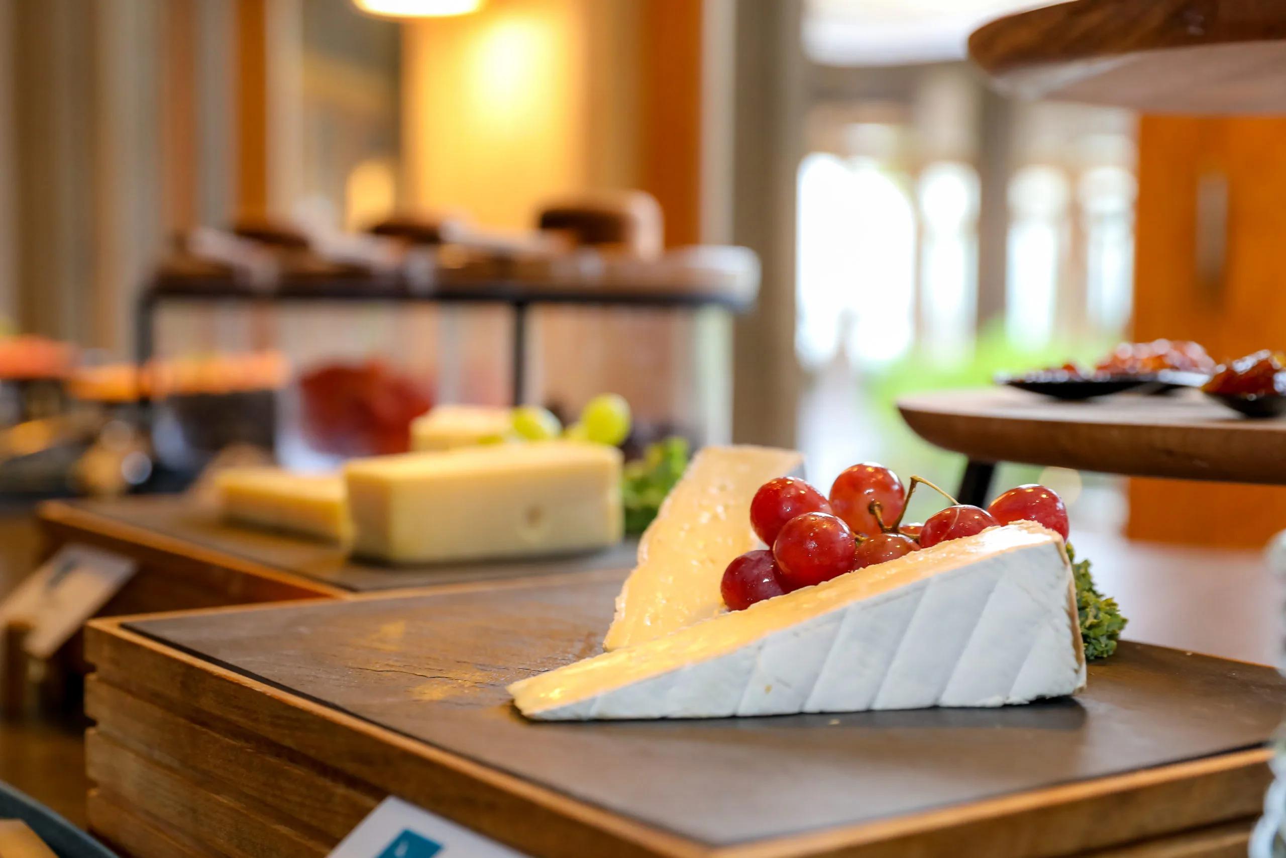 A wedge of brie topped with fresh grapes, part of a cheese selection laid out on a slate board