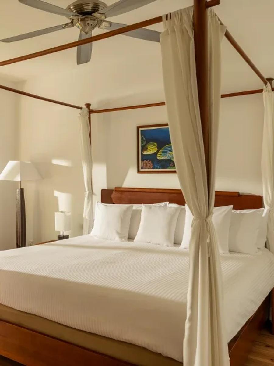 Beach Bungalow bedroom with a four-poster canopy bed, white bedding, and a daybed with a mustard-yellow cushion beneath a garden-facing window