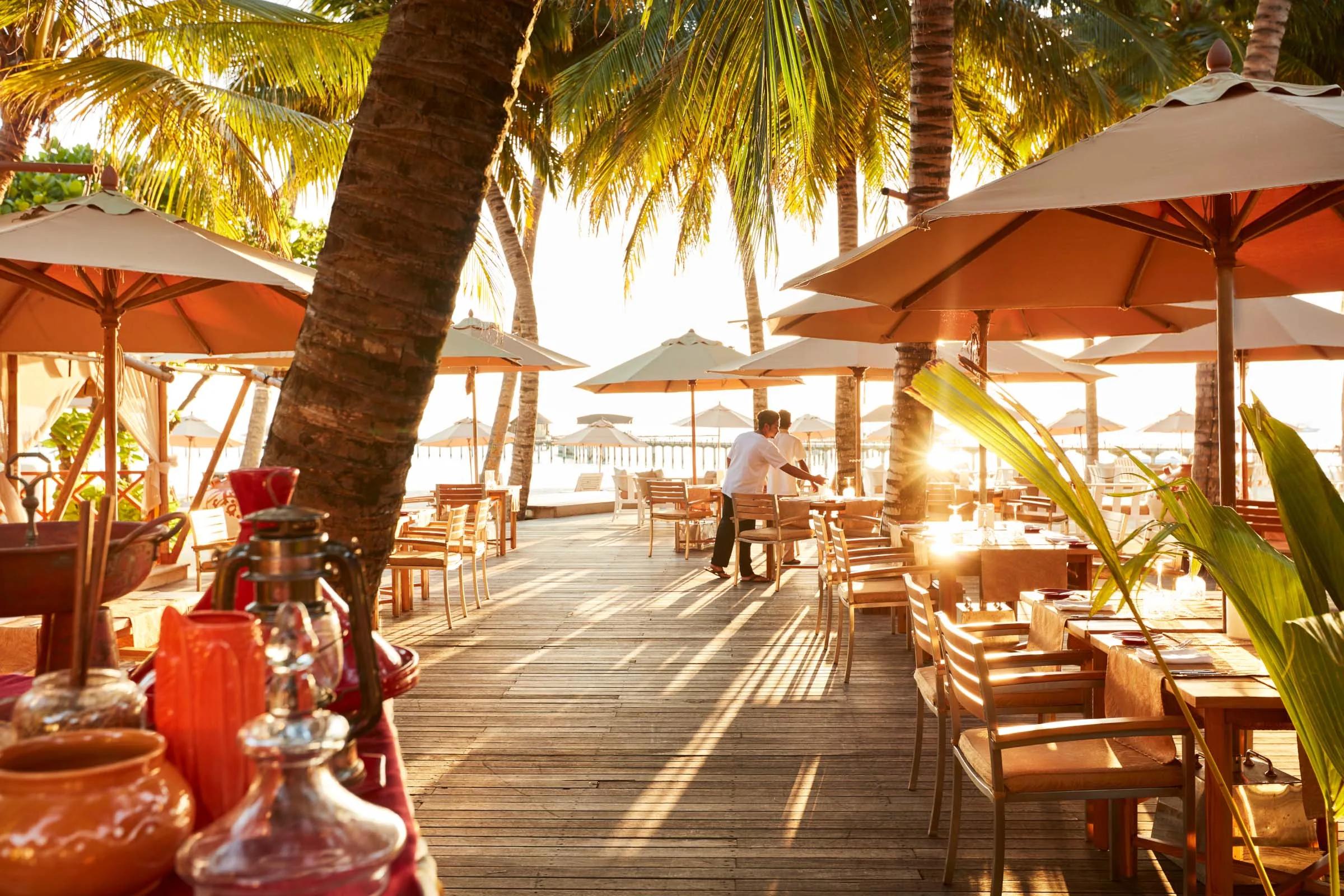 Beachfront dining tables under orange umbrellas at sunset, representative of Iru Fushi's adults-only beach club — dedicated Beach Club photography to follow