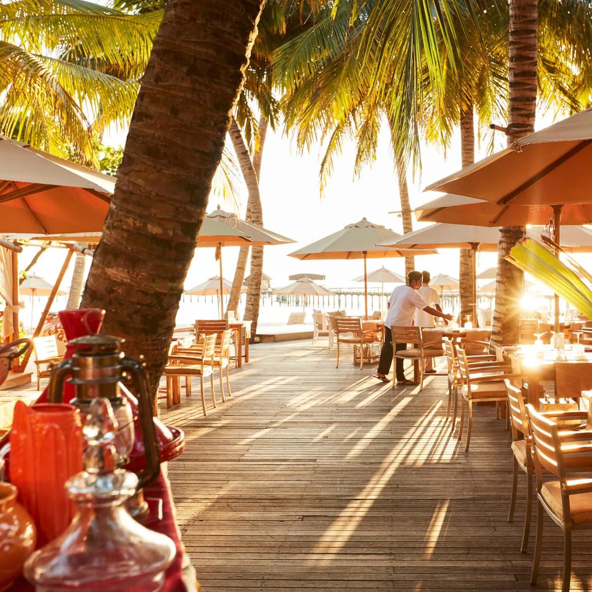 Beachfront dining tables under orange umbrellas at sunset, representative of Iru Fushi's adults-only beach club — dedicated Beach Club photography to follow