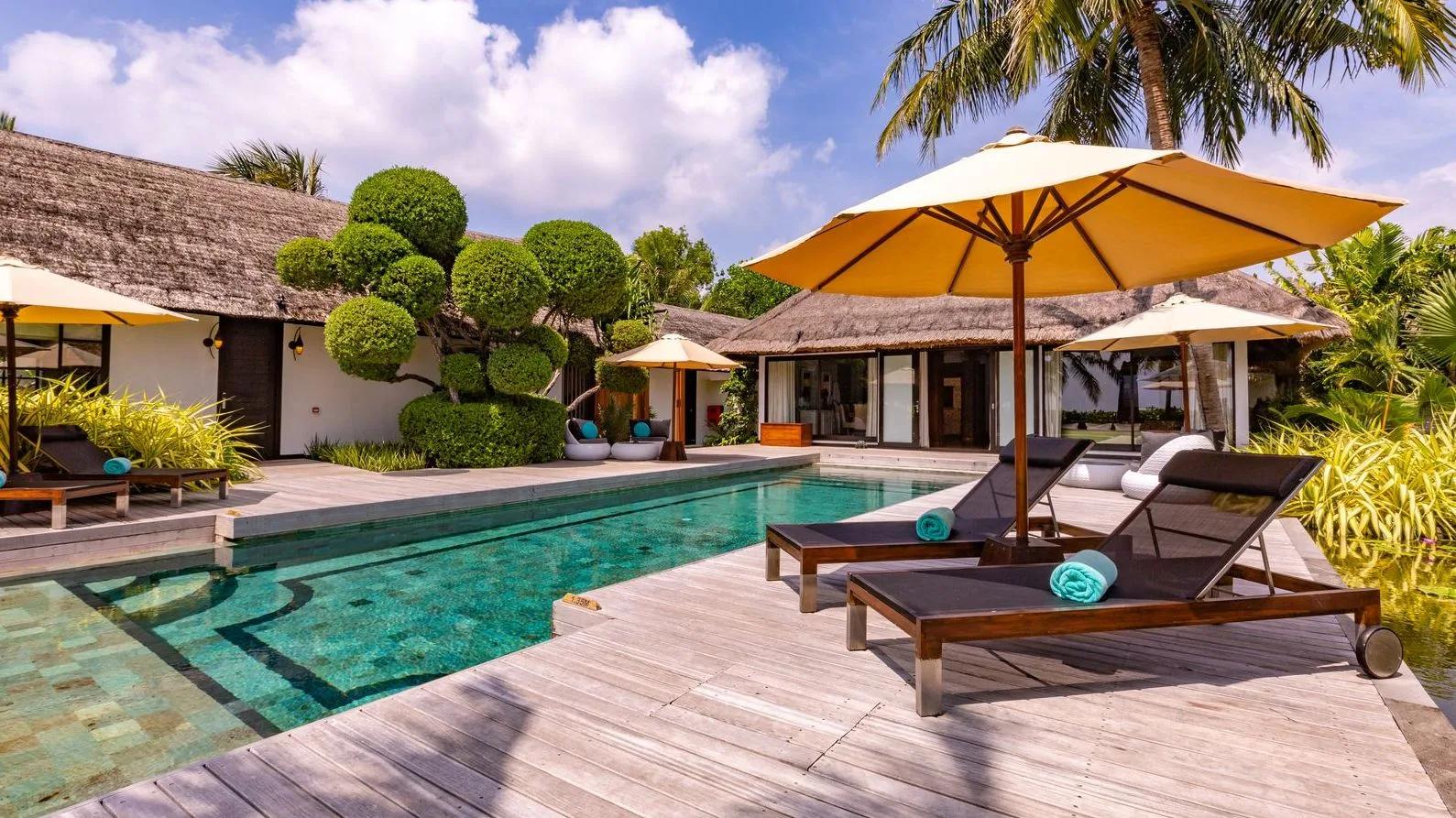 The Royal RESERVE's long lap pool and terrace, bordered by clipped topiary and sun loungers under a thatched roof