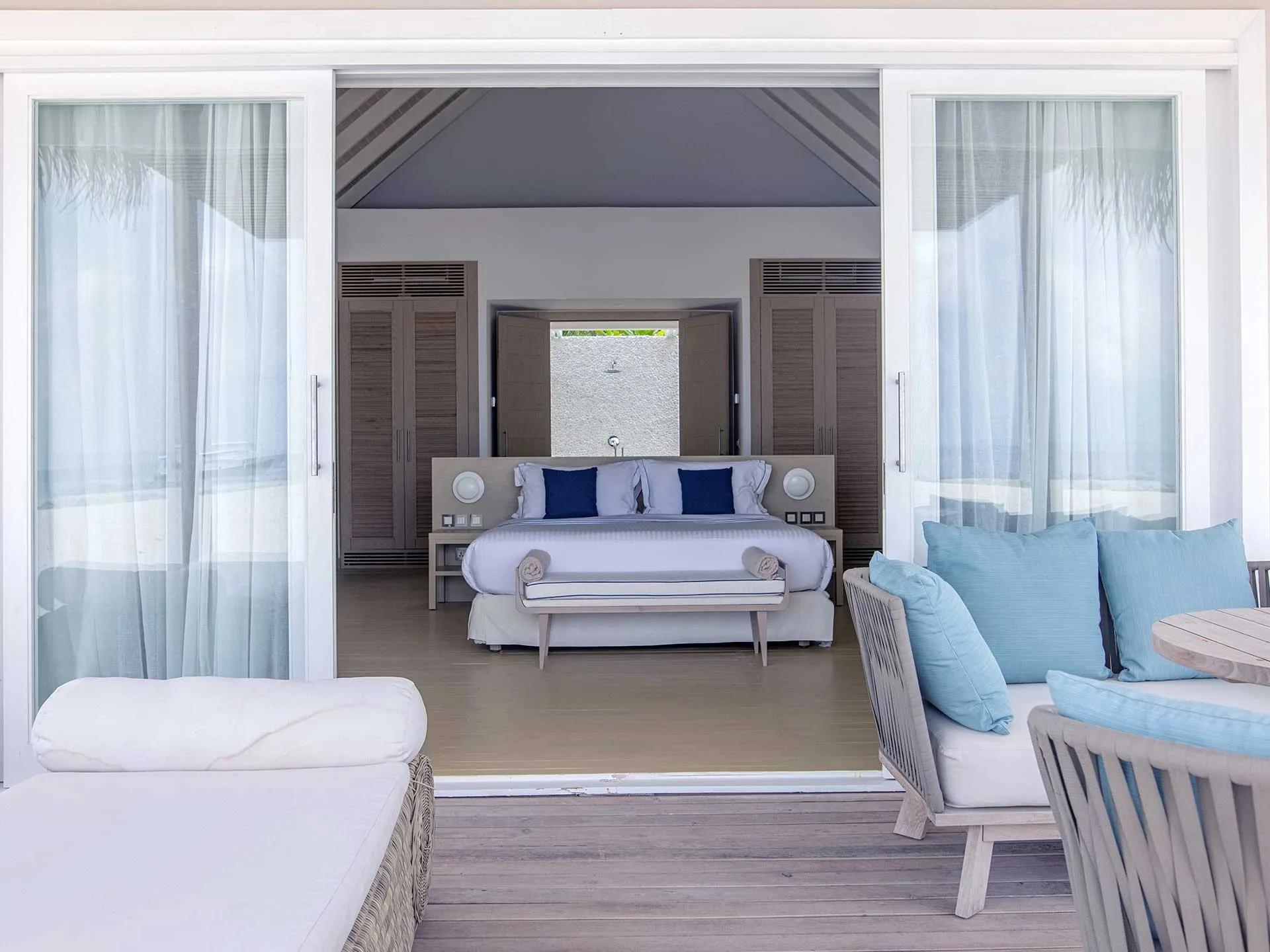 A Beach Villa's outdoor lounge looking back through open sliding doors to the bedroom and outdoor shower at Baglioni Maldives