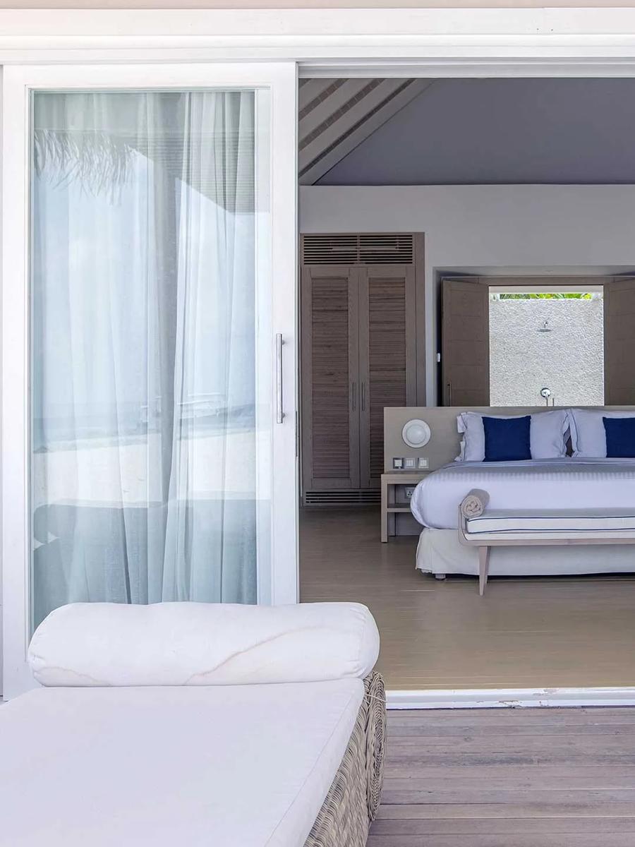 A Beach Villa's outdoor lounge looking back through open sliding doors to the bedroom and outdoor shower at Baglioni Maldives