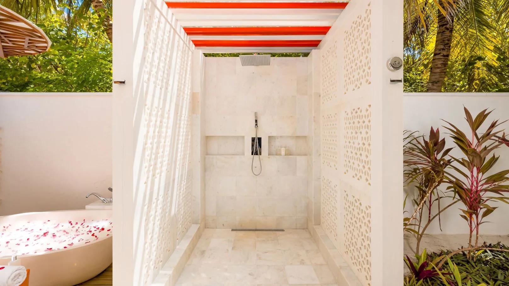 An alfresco stone shower beside a bathtub scattered with rose petals, open to the garden