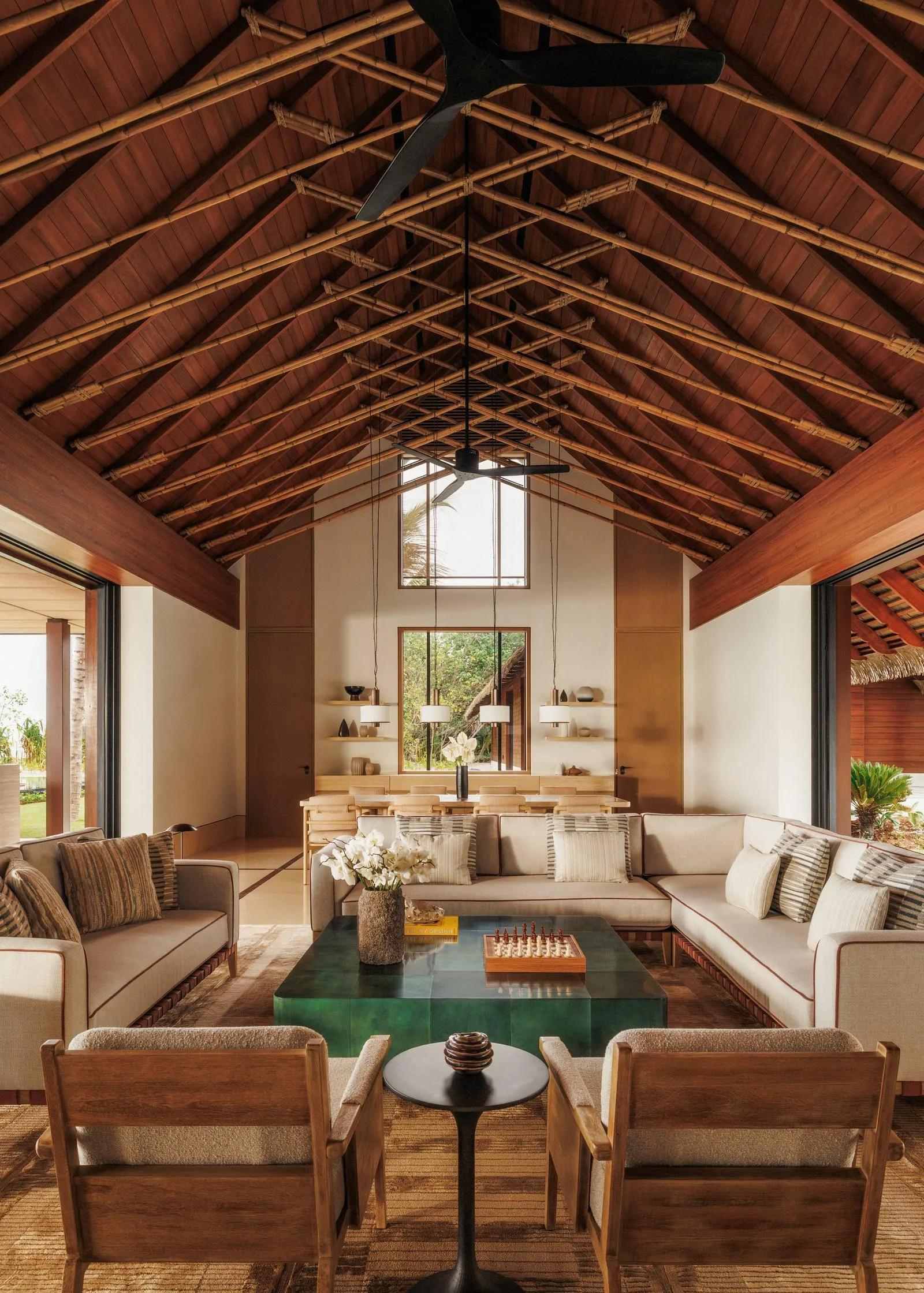A large open-plan living and dining room inside a Grand Residence at One&Only Reethi Rah, with a vaulted bamboo ceiling and a table set for eight