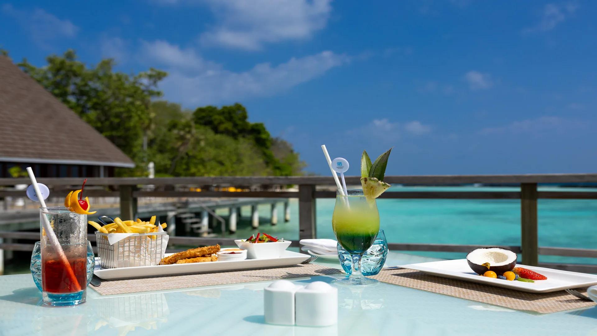 Cocktails and a plate of fries and fish goujons on a table at Sea Breeze, the jetty and lagoon visible beyond the rail
