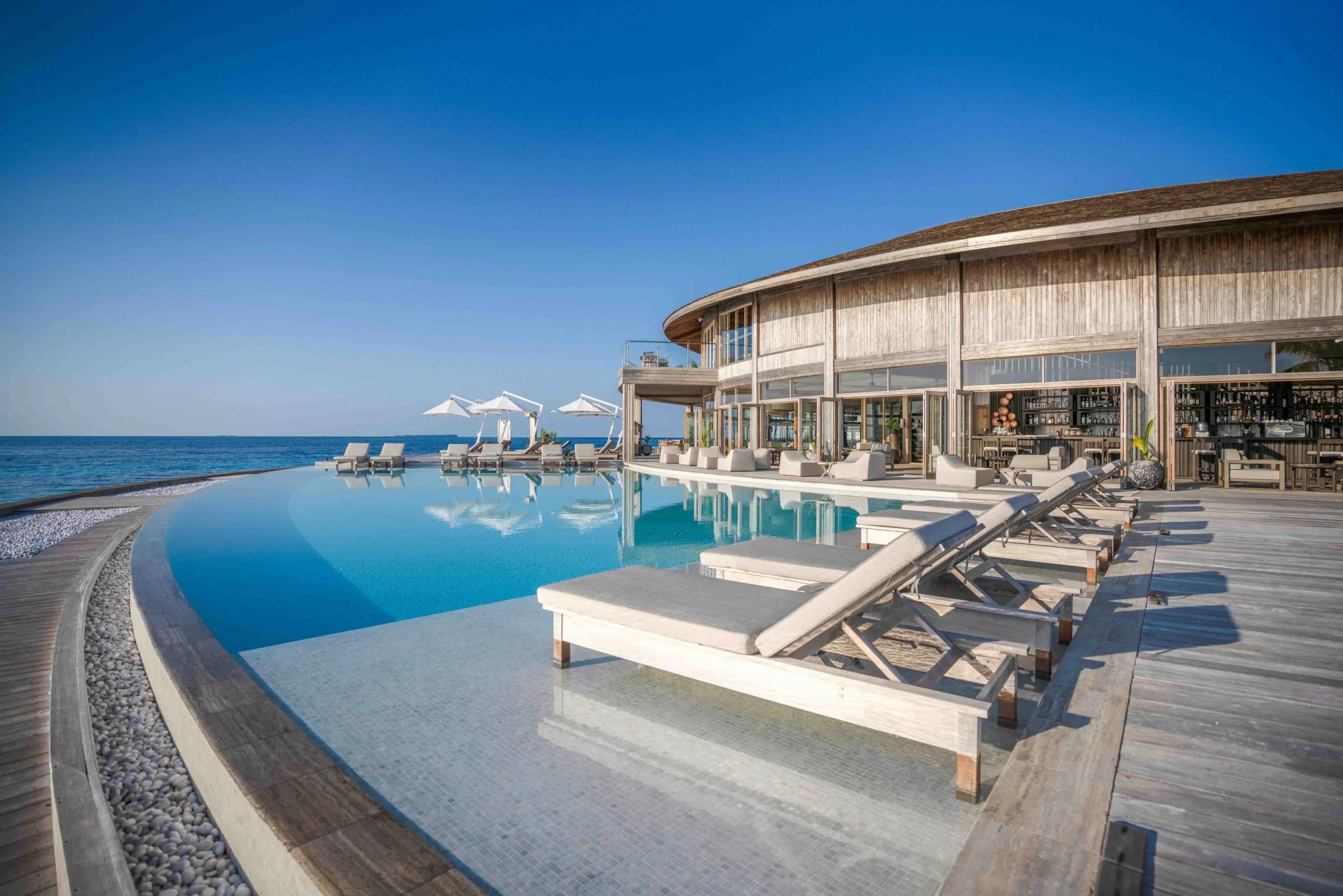 Ufaa Bar's round, shingle-roofed building beside the main pool, sun loungers along the deck and a stocked bar visible through the open walls