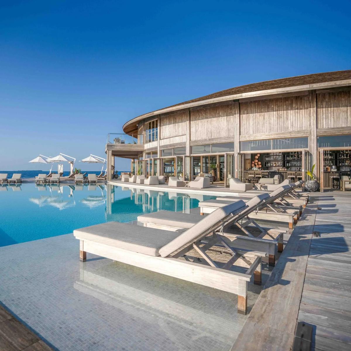 Ufaa Bar's round, shingle-roofed building beside the main pool, sun loungers along the deck and a stocked bar visible through the open walls