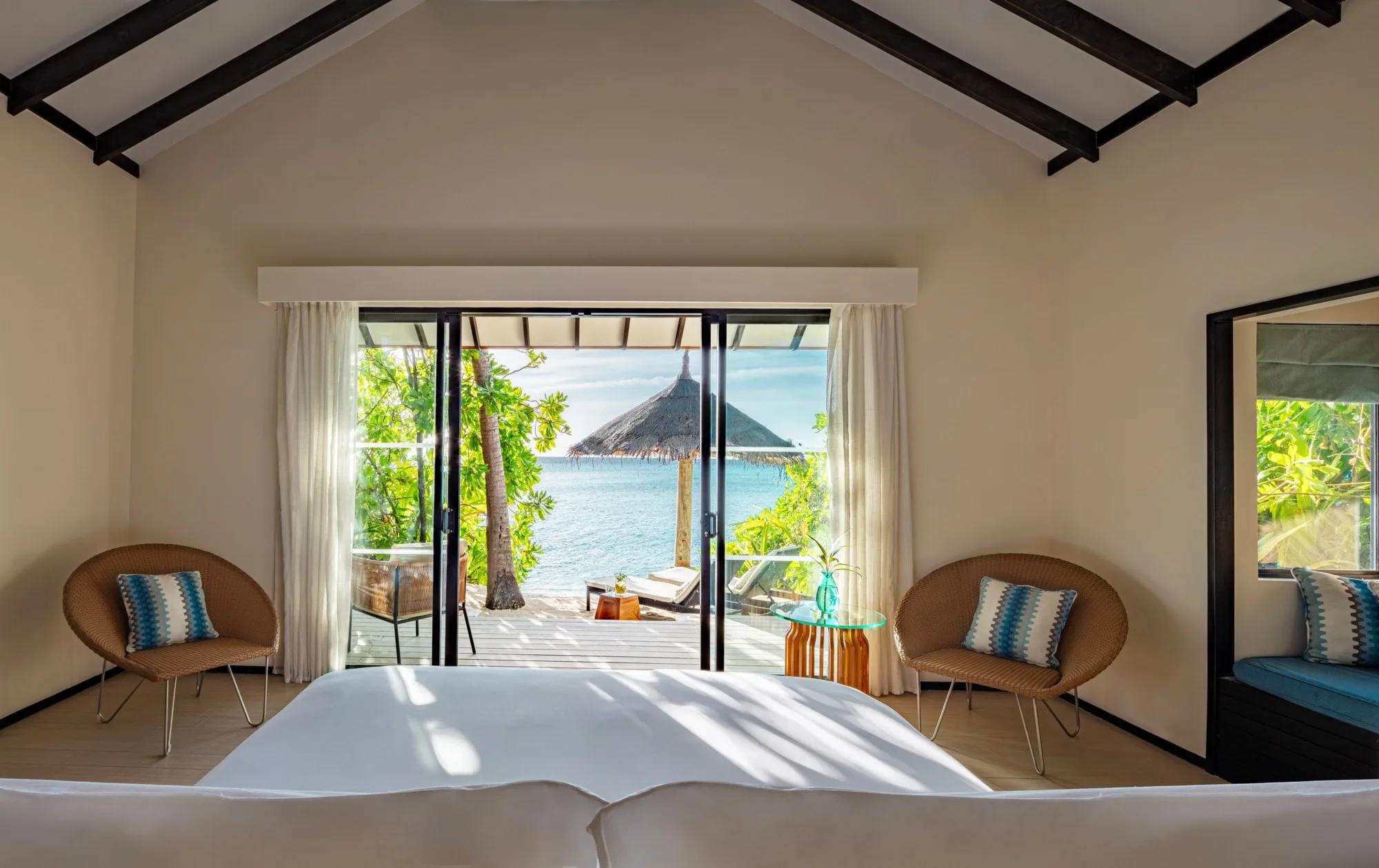 A view from a Beach Villa with Private Pool's bed out through sliding doors to a thatched beach umbrella and the lagoon beyond
