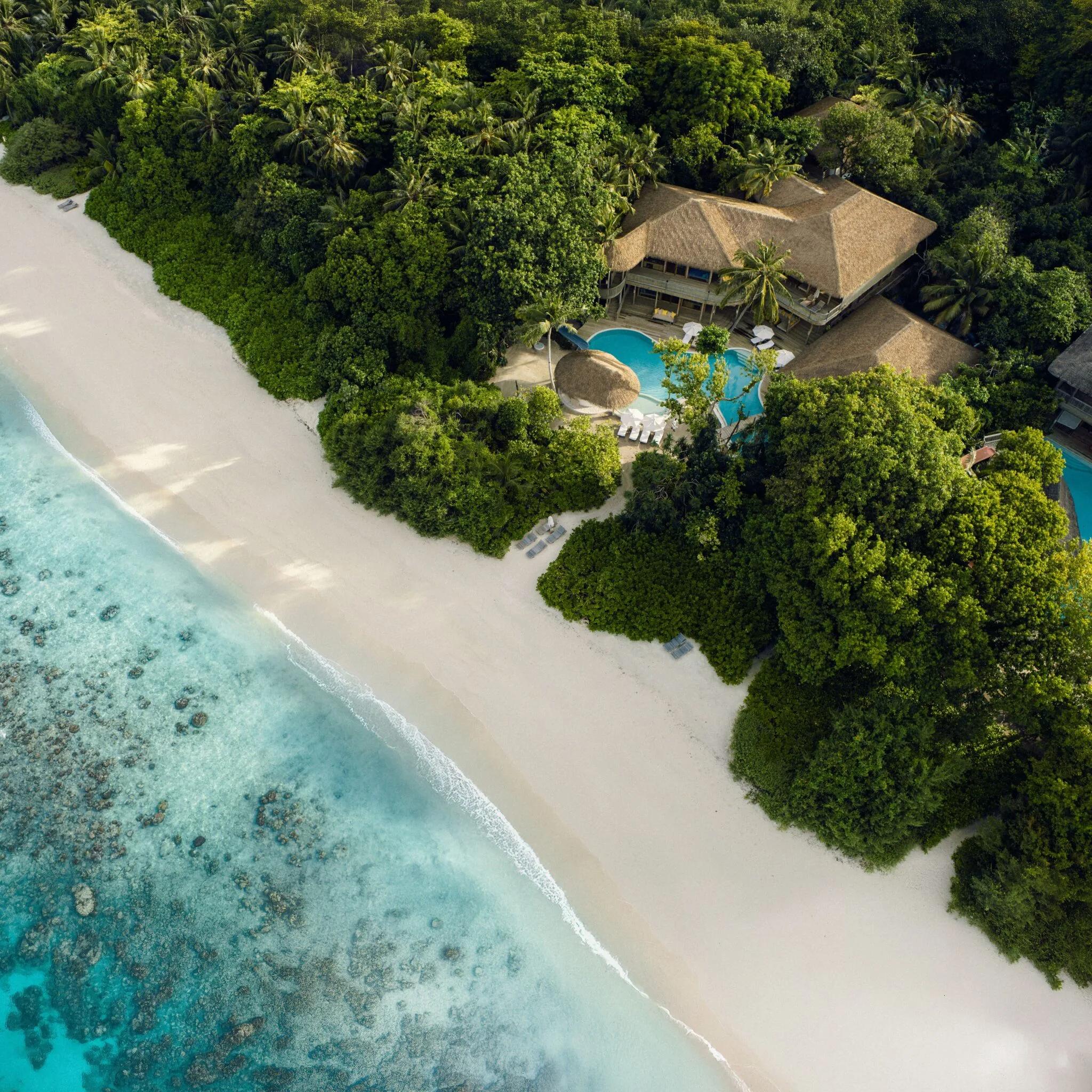 An aerial view of Villa 37, one of Soneva Fushi's two 6-Bedroom Residences, its thatched roofs and pool set steps from the beach and reef