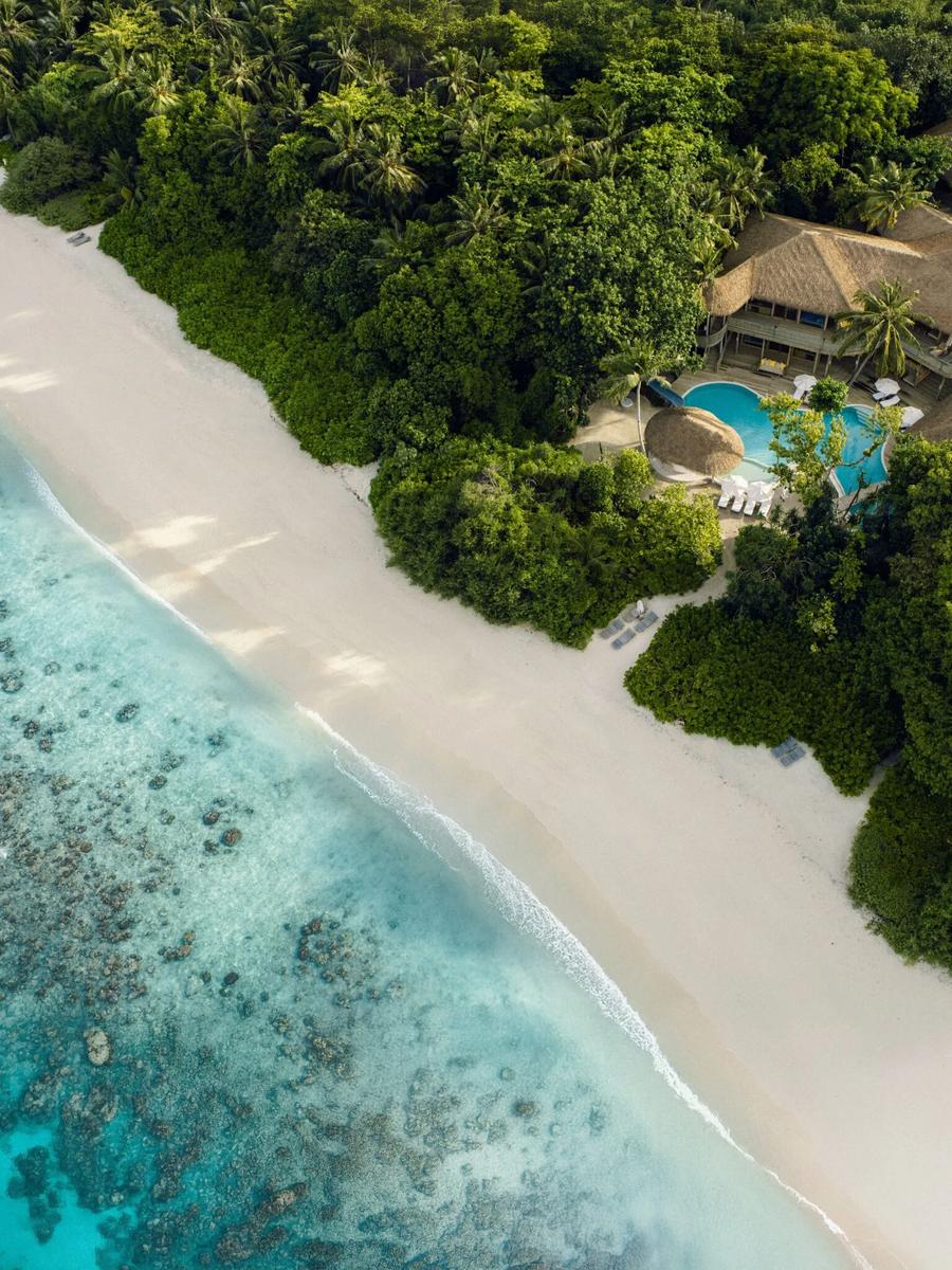 An aerial view of Villa 37, one of Soneva Fushi's two 6-Bedroom Residences, its thatched roofs and pool set steps from the beach and reef