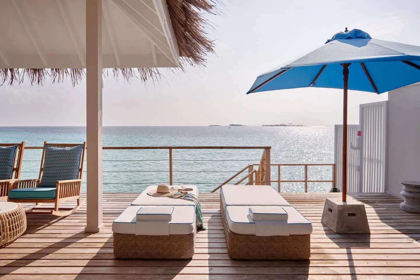 A Lagoon Villa's shaded overwater deck, with a wooden jetty and steps leading down toward the water and a small island on the horizon