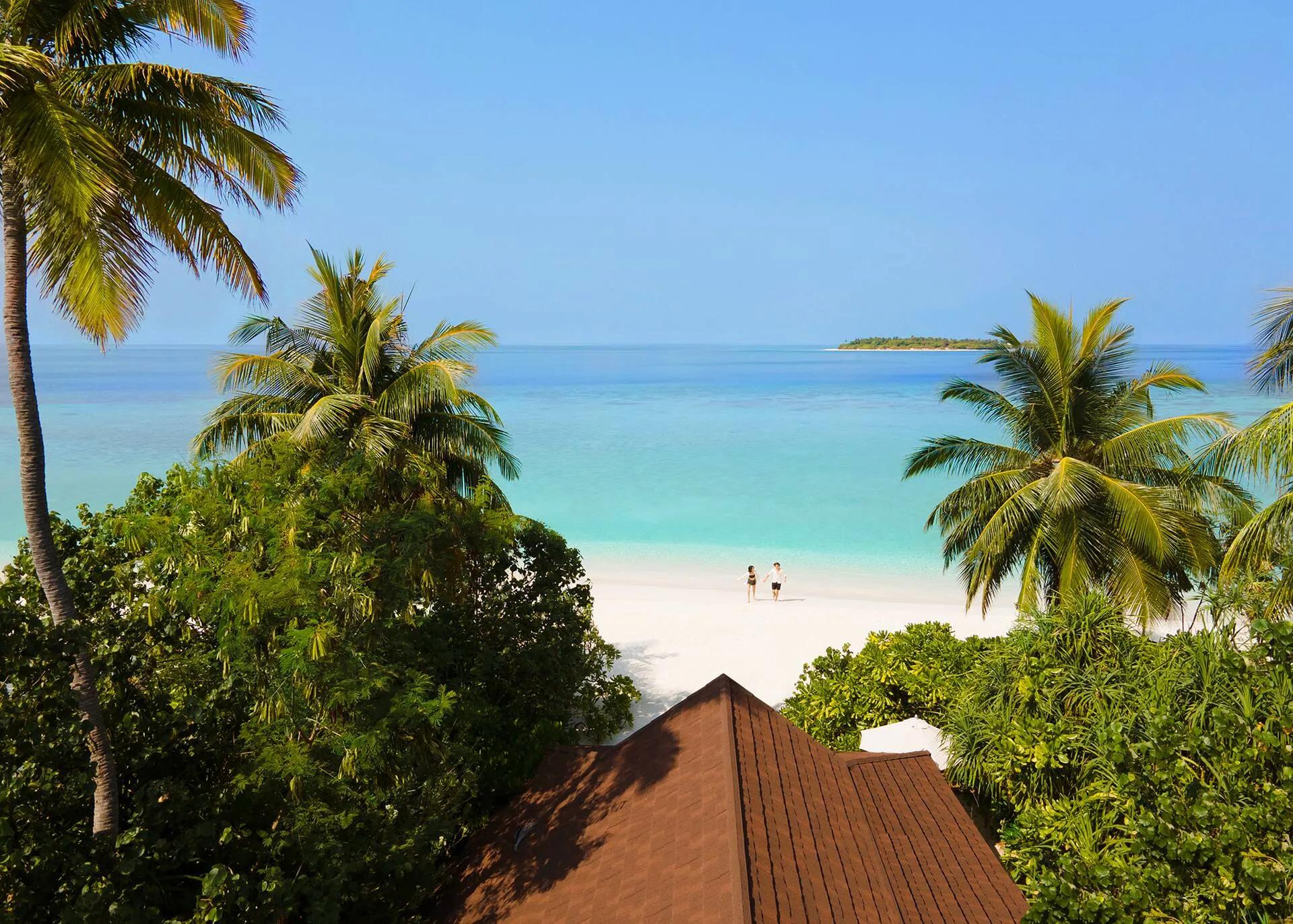 View from an Ocean Beach Villa's terrace through palm trees toward the beach and a small island on the horizon