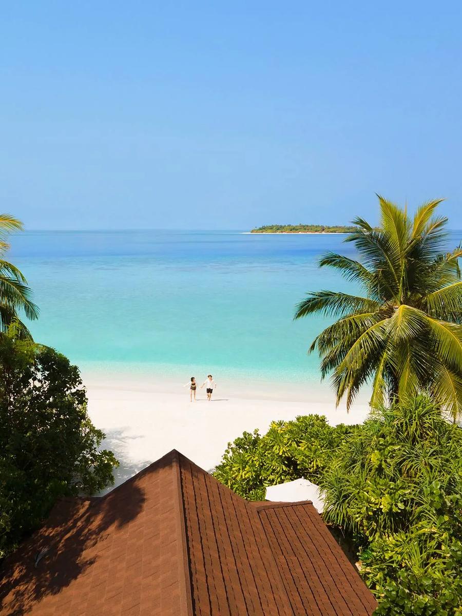 View from an Ocean Beach Villa's terrace through palm trees toward the beach and a small island on the horizon