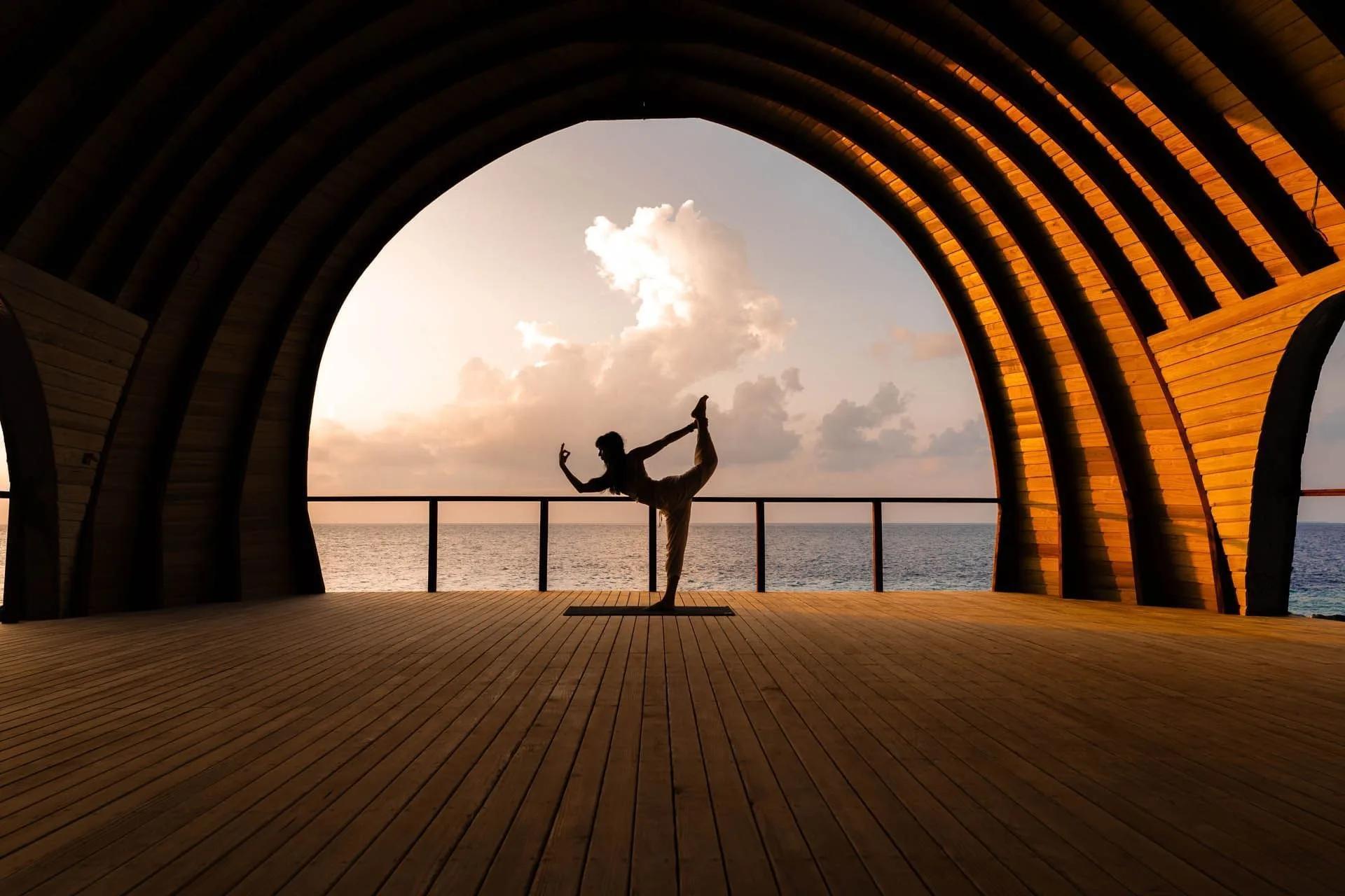 A silhouetted yoga pose inside Kandu Spa's dedicated overwater yoga pavilion at sunset