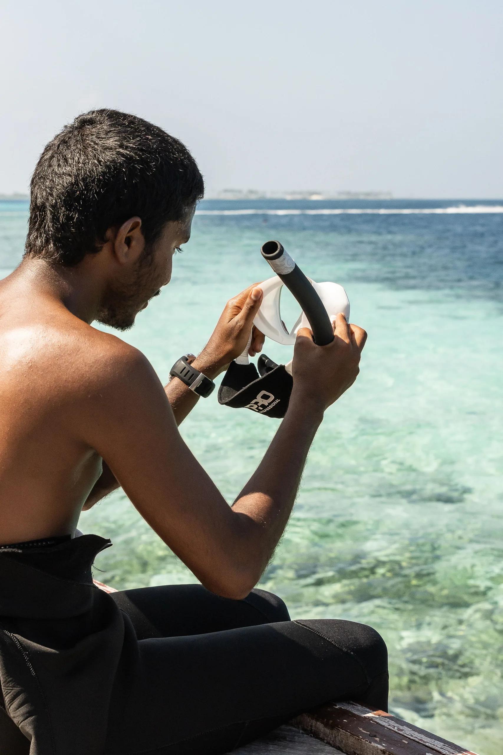 A guest fitting a snorkel mask and snorkel on a boat, clear turquoise reef water ahead