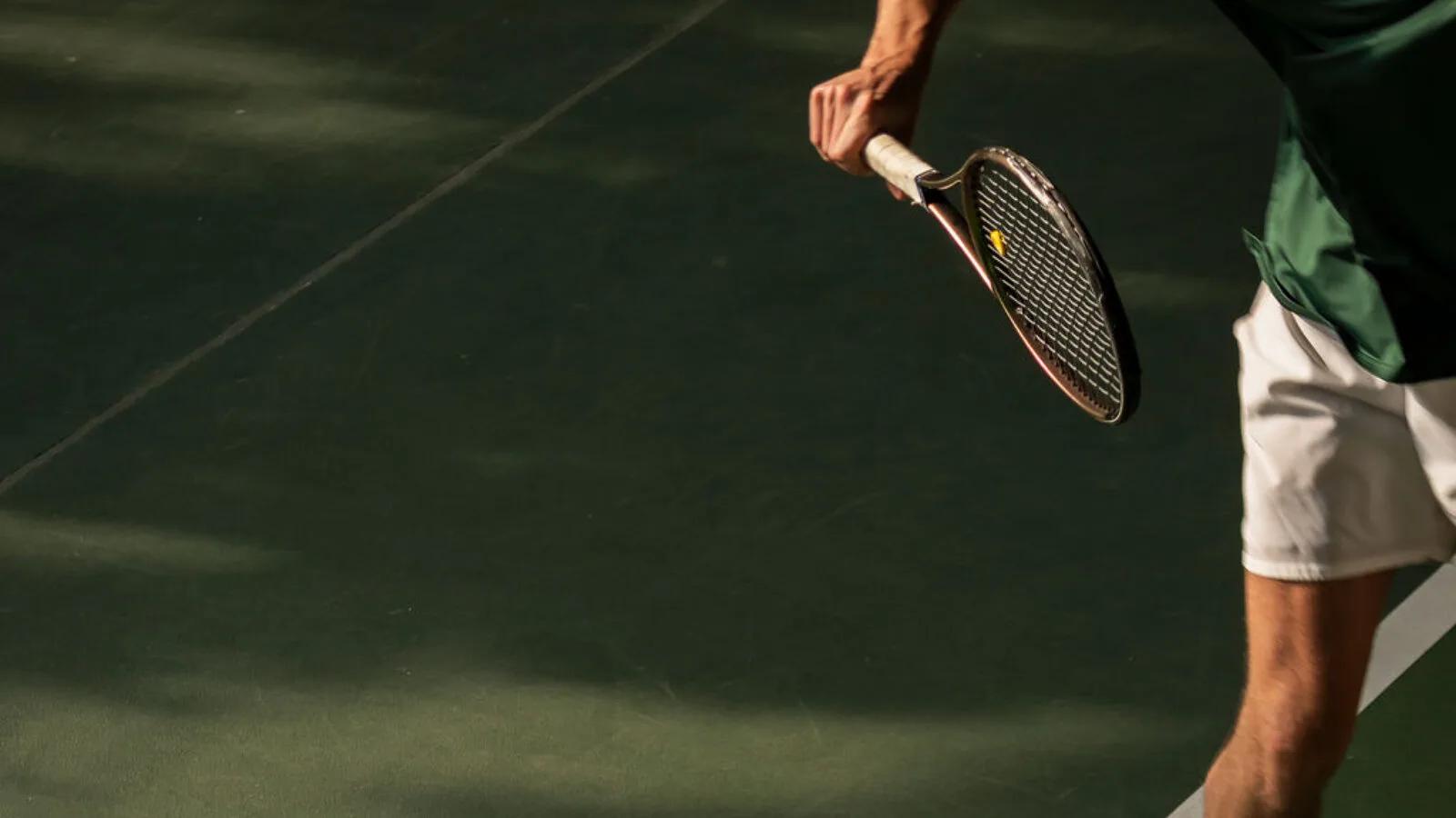 A player's racket and serving arm, mid-motion on one of Soneva Fushi's open-air tennis courts