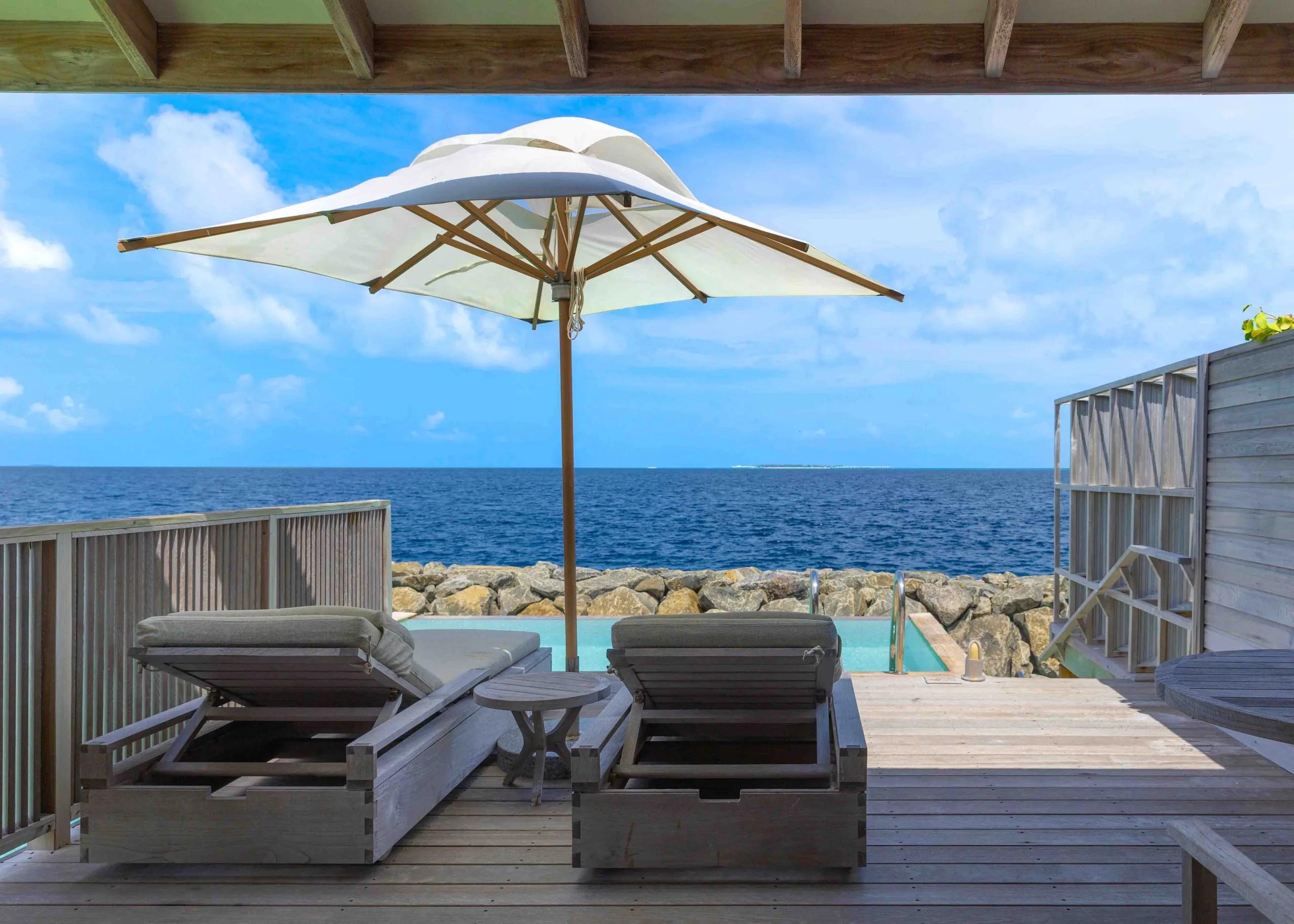 A private plunge pool and shaded lounge deck at the water's edge, a rocky breakwater and open ocean beyond