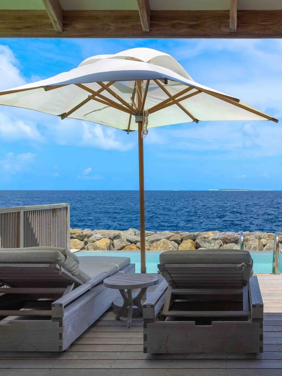 A private plunge pool and shaded lounge deck at the water's edge, a rocky breakwater and open ocean beyond