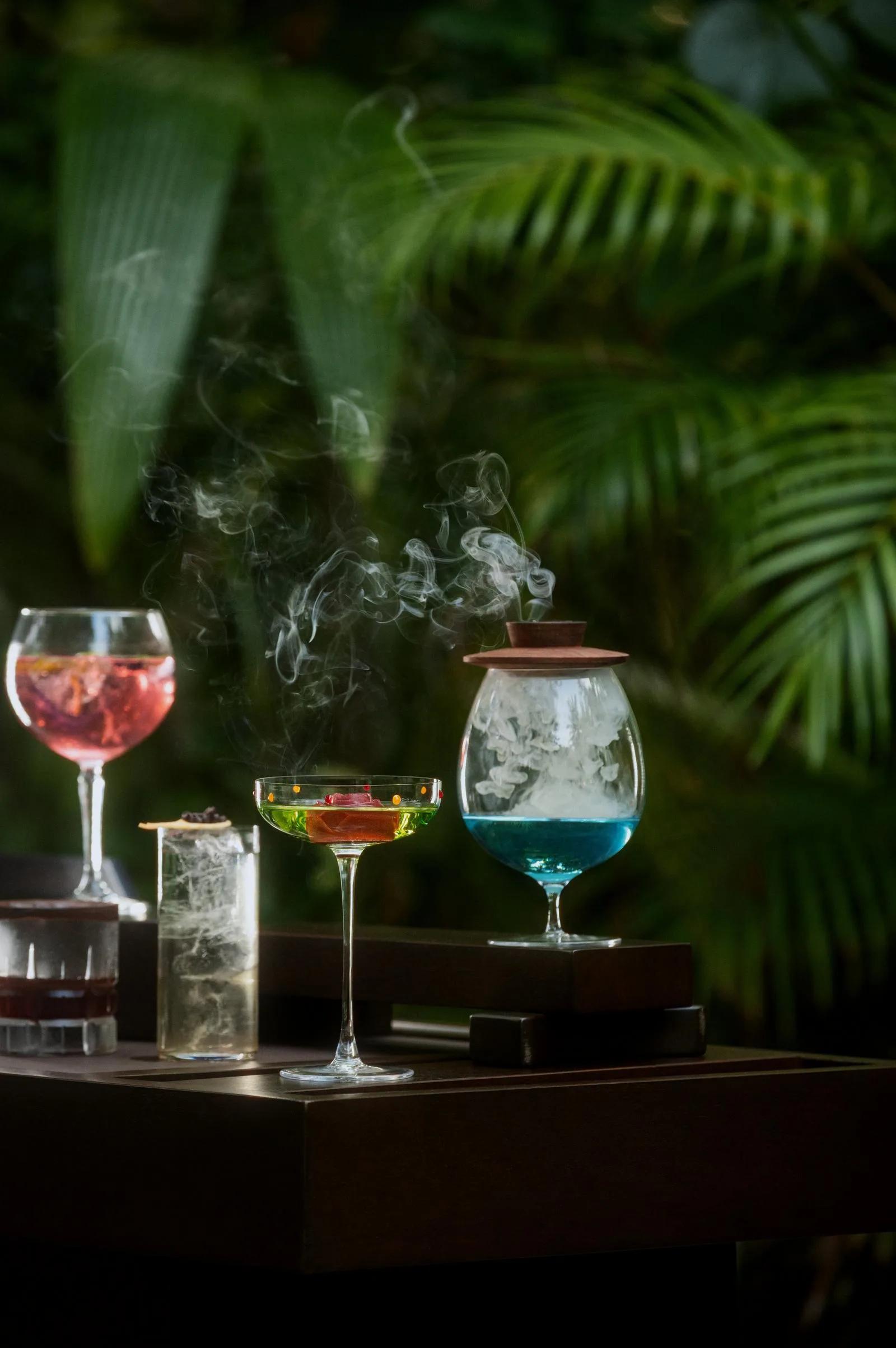 Cocktails, one served smoking under a glass dome, in a garden setting at One&Only Reethi Rah — standing in for Rah Bar, the resort's day-to-evening bar, since no dedicated Rah Bar photograph was collected