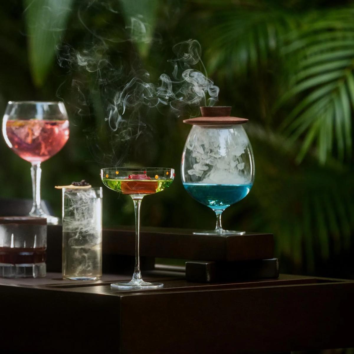 Cocktails, one served smoking under a glass dome, in a garden setting at One&Only Reethi Rah — standing in for Rah Bar, the resort's day-to-evening bar, since no dedicated Rah Bar photograph was collected