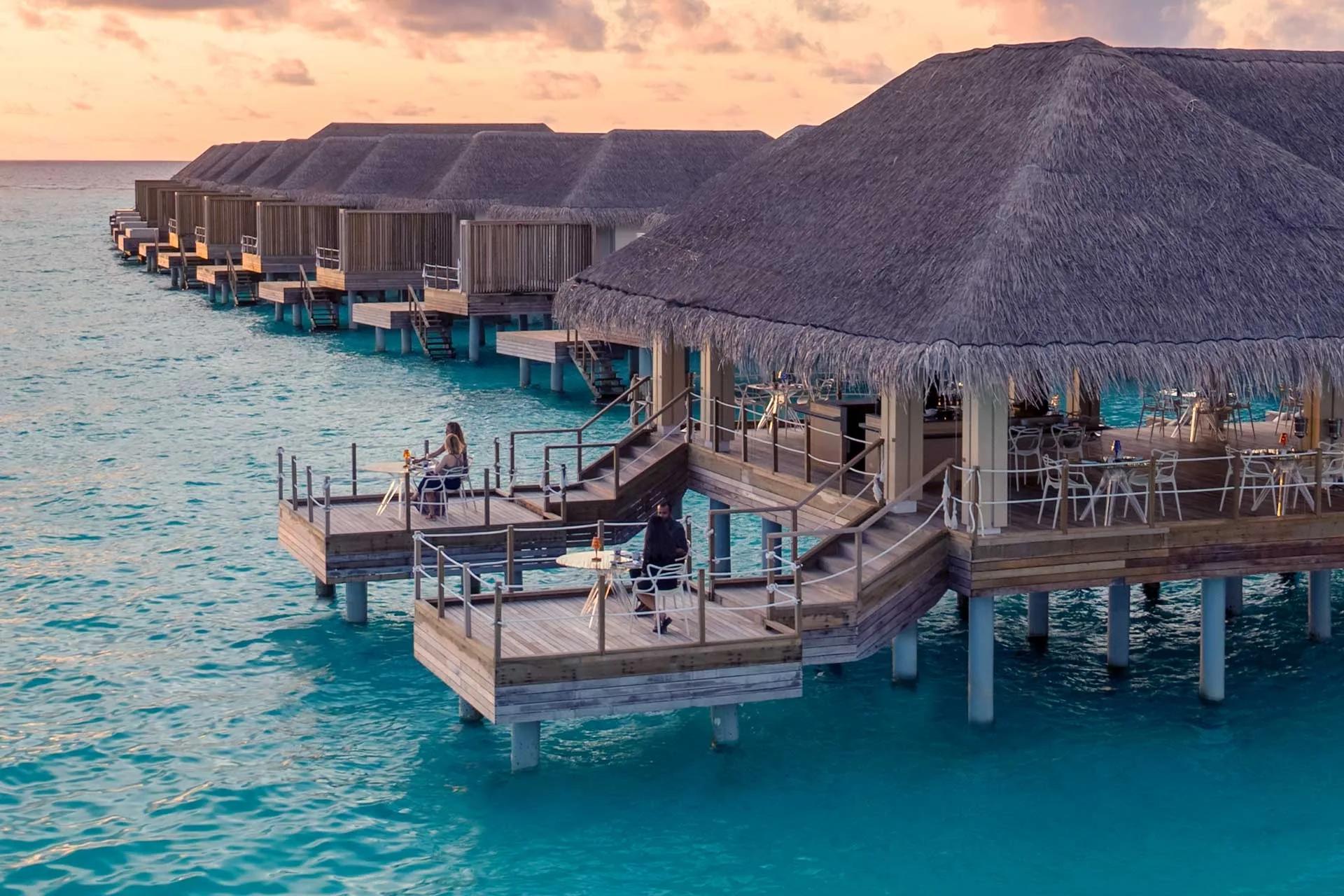 Yama's overwater dining deck at dusk, guests seated around an open teppanyaki bar lit by flame