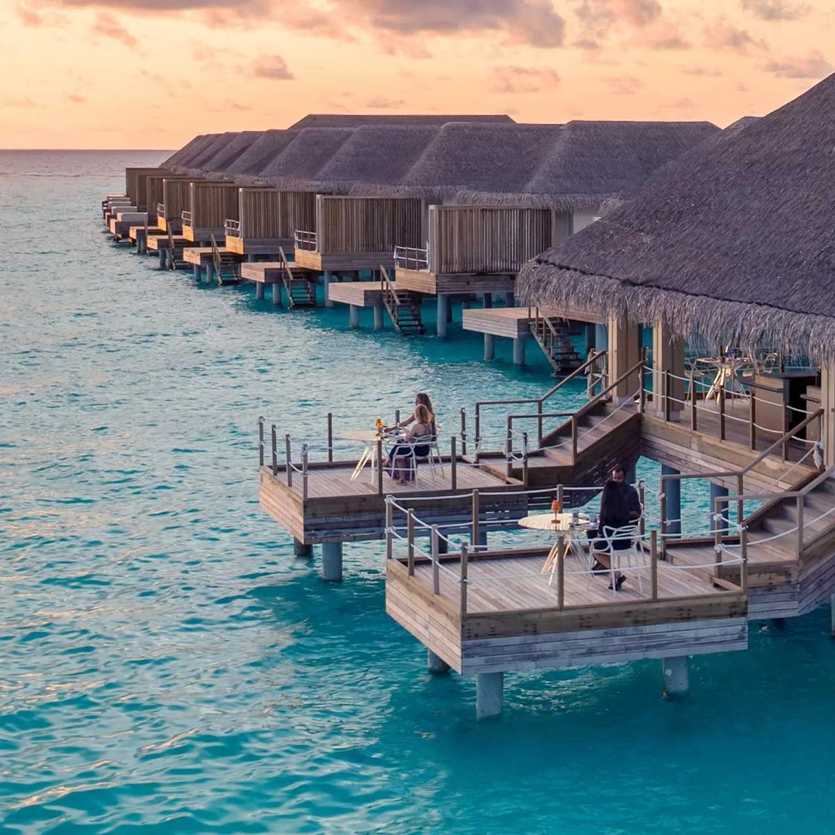 Yama's overwater dining deck at dusk, guests seated around an open teppanyaki bar lit by flame