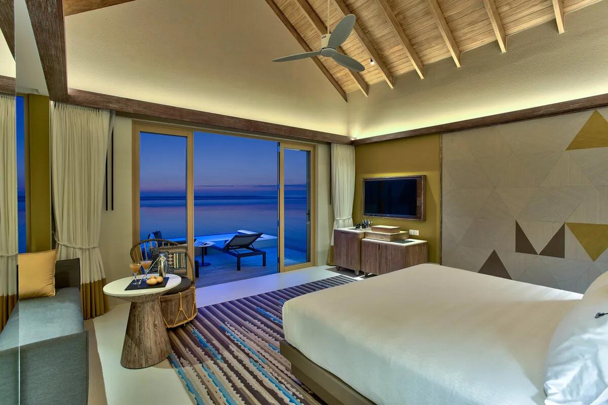 The Diamond Overwater Private Pool Villa's bedroom, sliding doors opening onto its deck and plunge pool over the lagoon