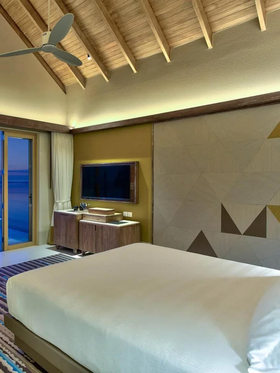 The Diamond Overwater Private Pool Villa's bedroom, sliding doors opening onto its deck and plunge pool over the lagoon